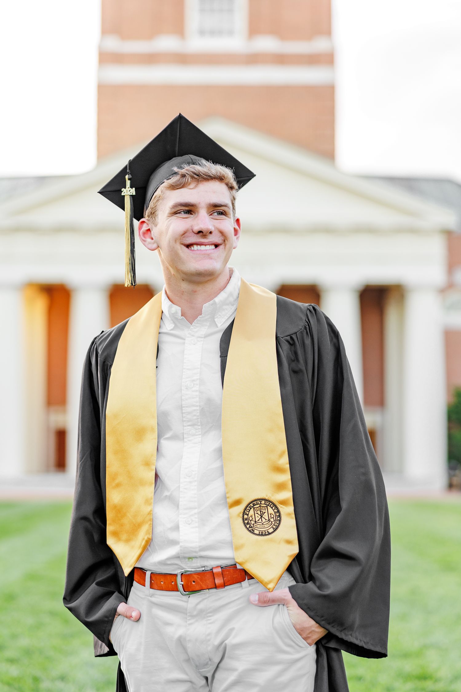 Graduate poses in black gown with gold stole against brick building backdrop at Wake Forest University with a Graduation Photographer