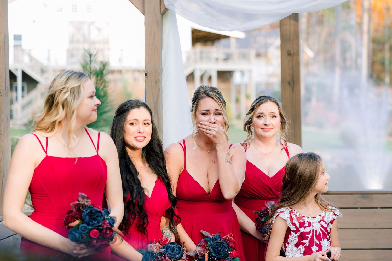 Bridesmaids in red dresses hold navy bouquets while posing together outdoors at the Barn at Union Grove Farm in Chapel Hill