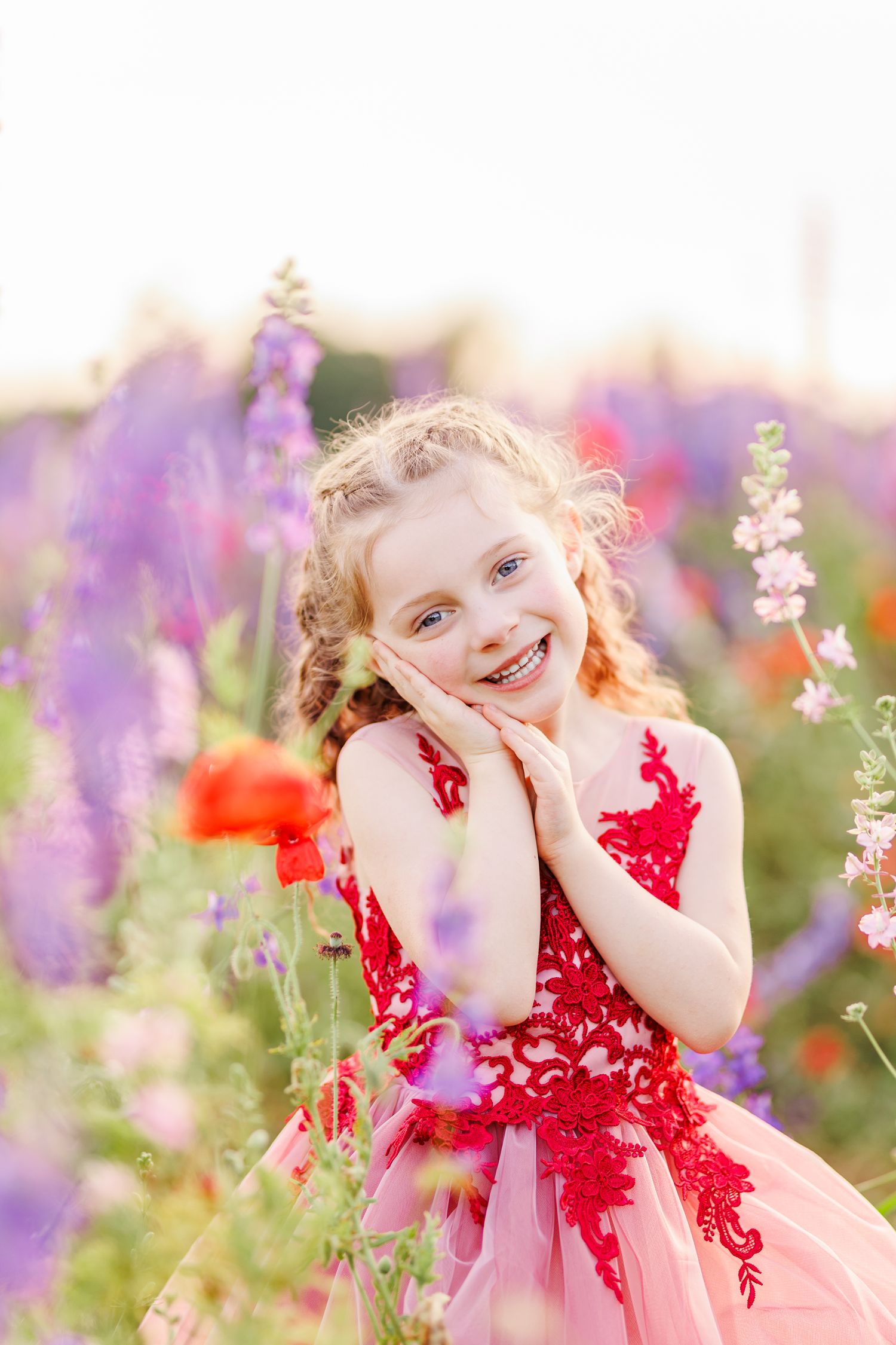 A red lace dress contrasts beautifully with purple and white flowers in a sunlit garden  in Winston Salem NC  with a Family Photographer