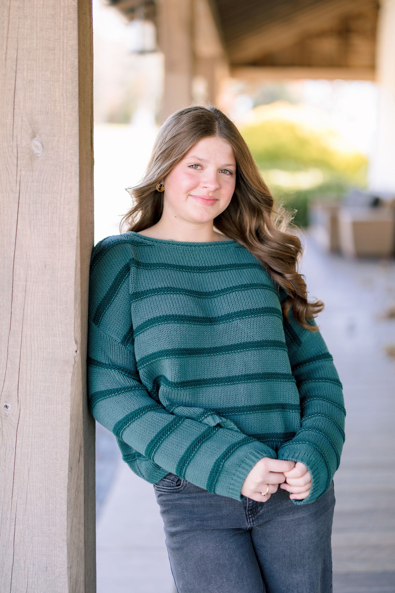 Woman in striped teal sweater poses against wooden backdrop in Summerfield NC  with a Family Photographer