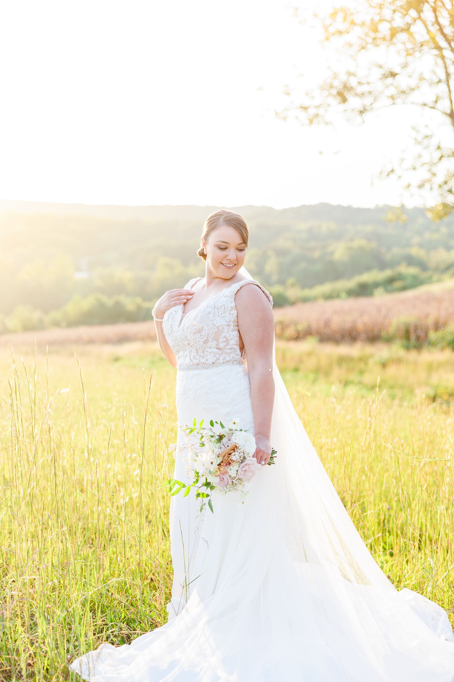 Flowing white wedding dress catches golden sunlight in a summer meadow.