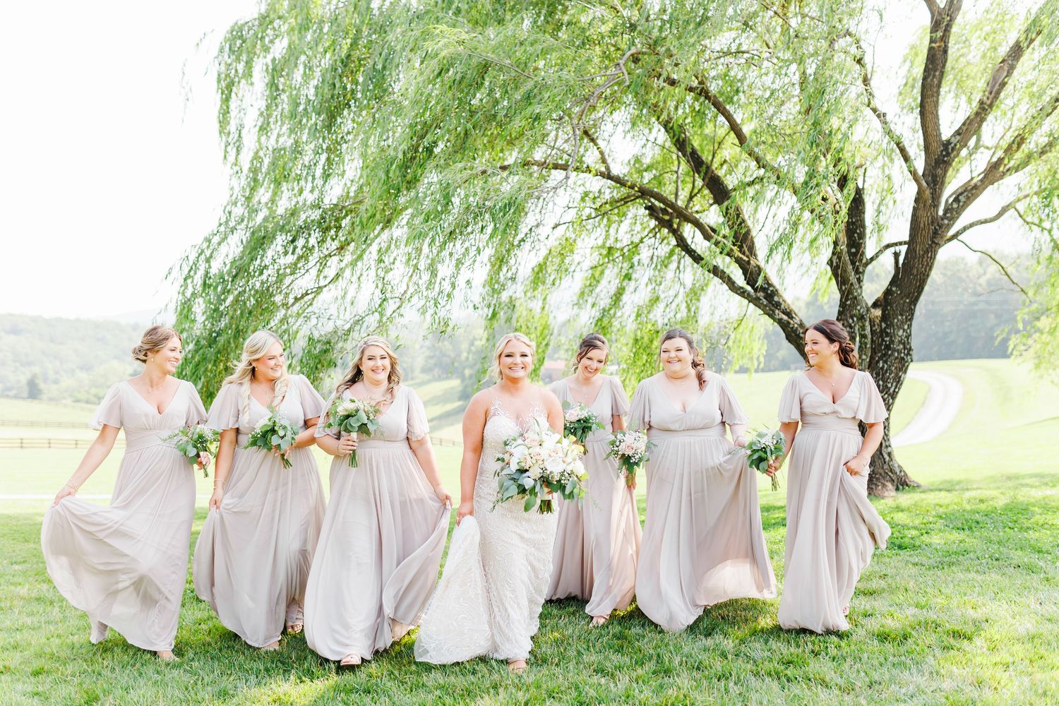 Bridesmaids in light gray dresses posing under a weeping willow tree at the Shilo with NC Wedding photographer