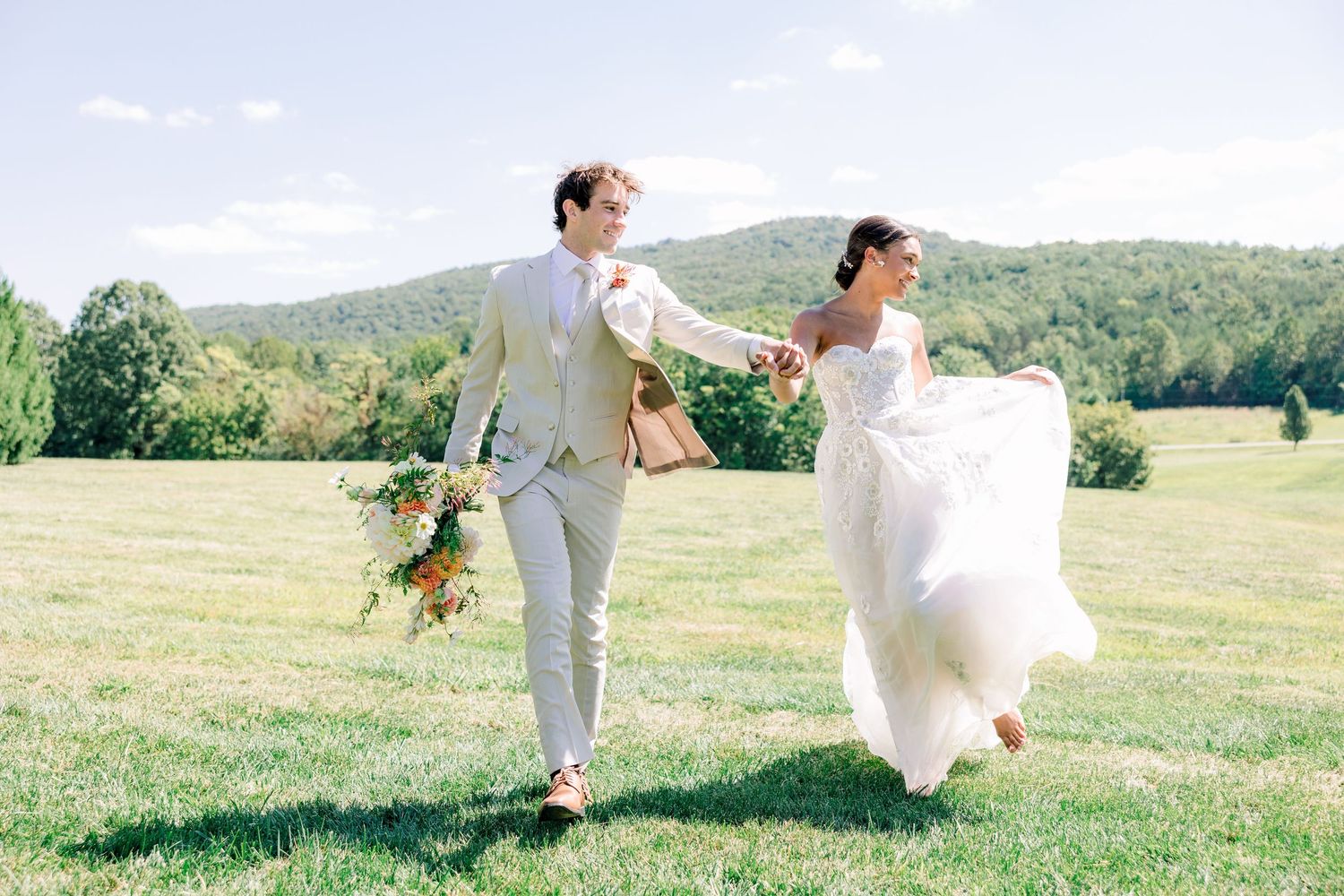 Wedding couple walking and dancing together in a sunny meadow with mountain views  with NC Wedding Photographer
