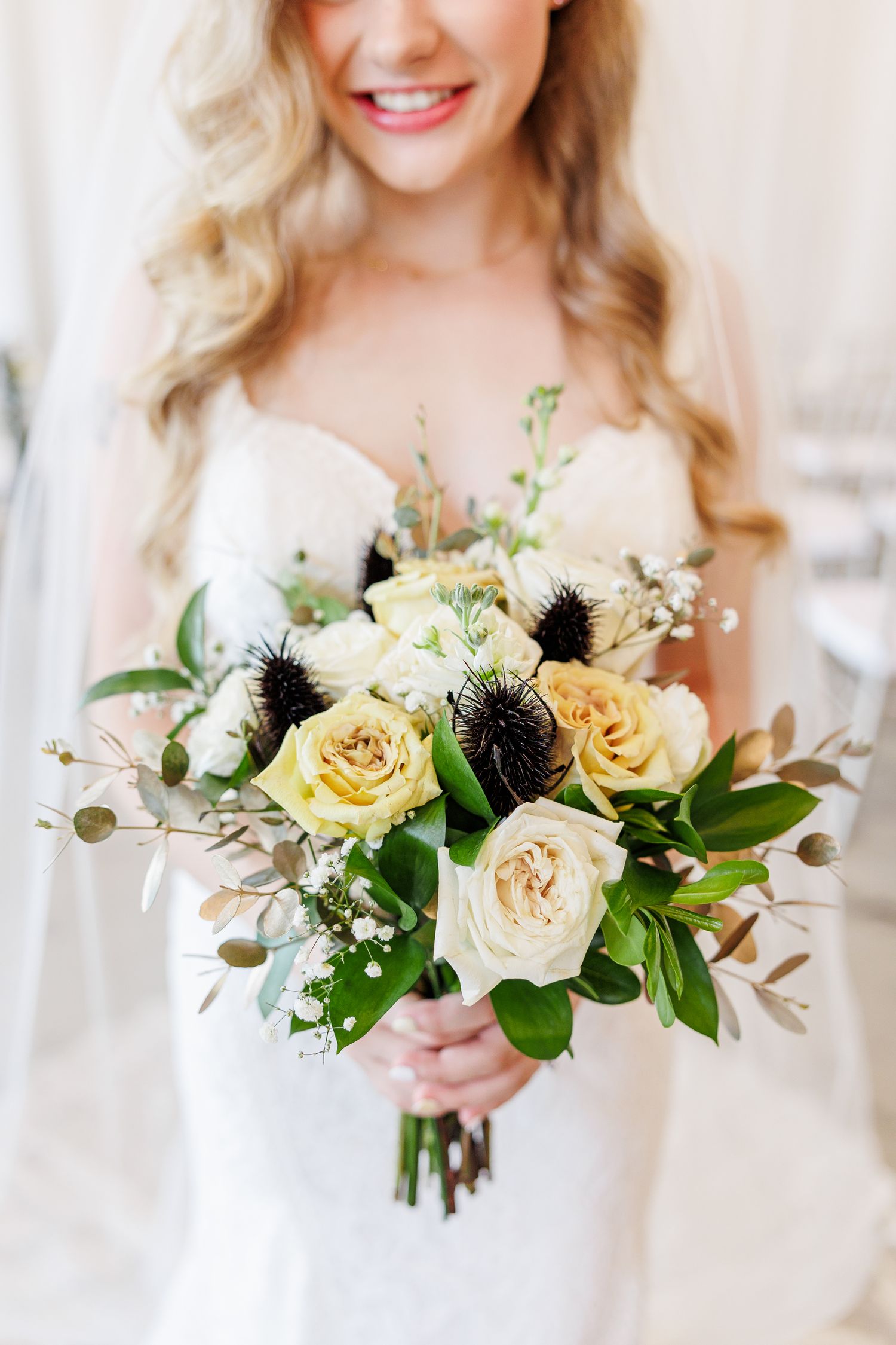 A beautiful bridal bouquet featuring cream and yellow roses with dark thistle accents and greenery with Kernersville Wedding Photographer