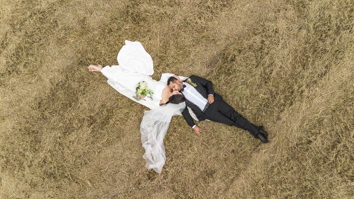 Aerial view of wedding couple lying on brown grass during outdoor photo session with NC Drone Wedding Photography