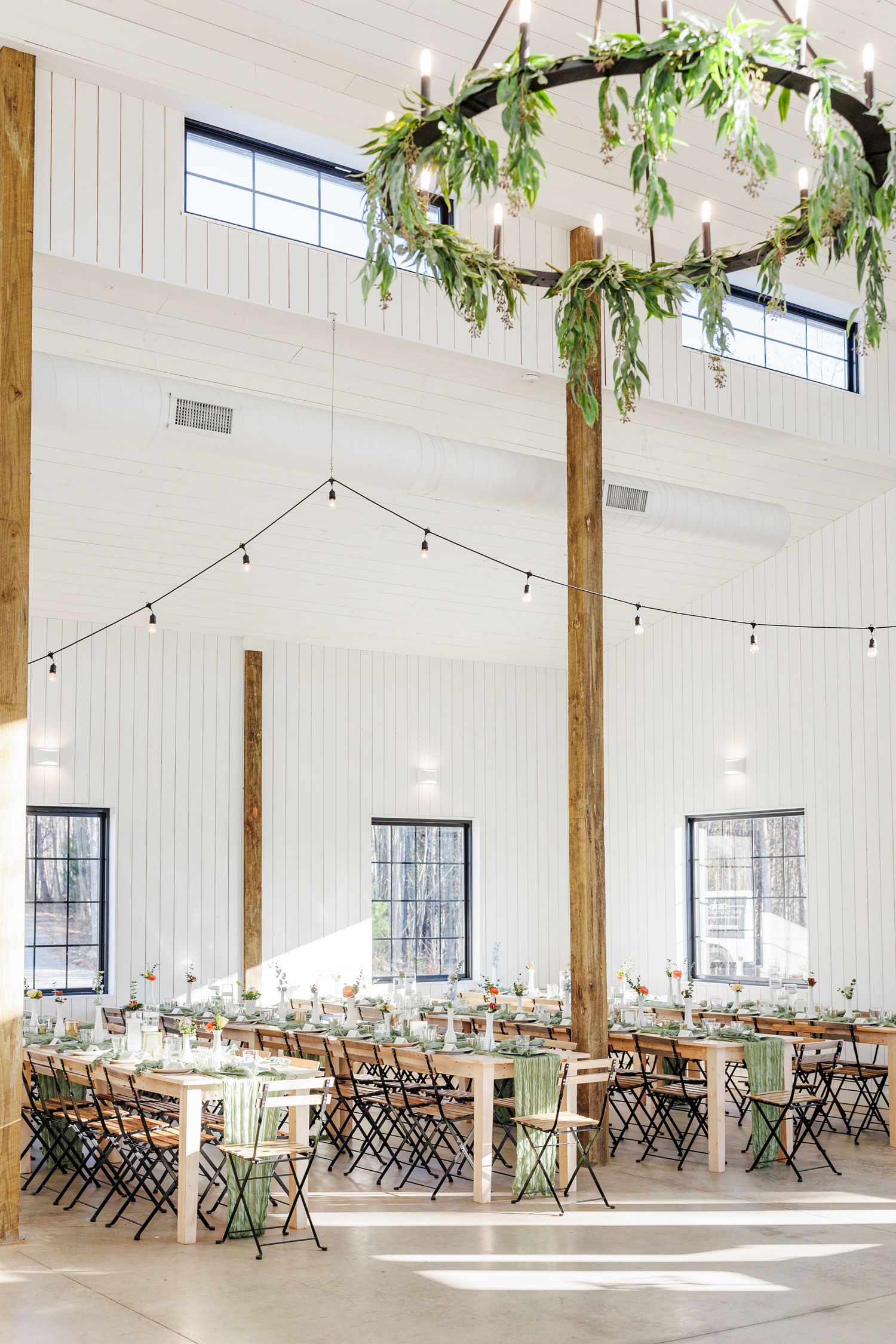 Light-filled rustic barn venue with wooden beams and string lights set up for an elegant wedding reception at Serre Vineyards with NC weddin