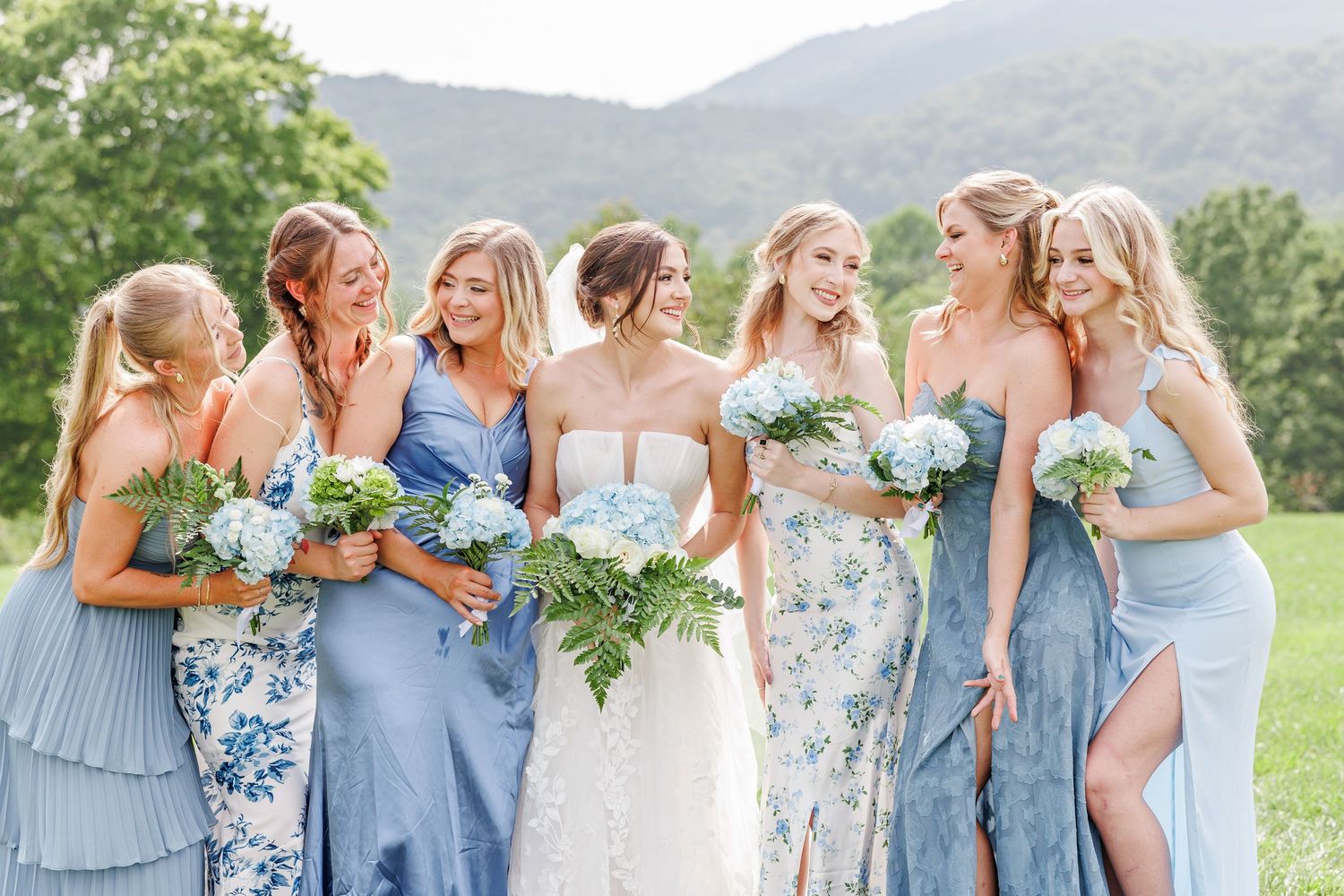 Bridesmaids in light blue dresses pose together holding bouquets against mountain backdrop with North Carolina Wedding Photographer