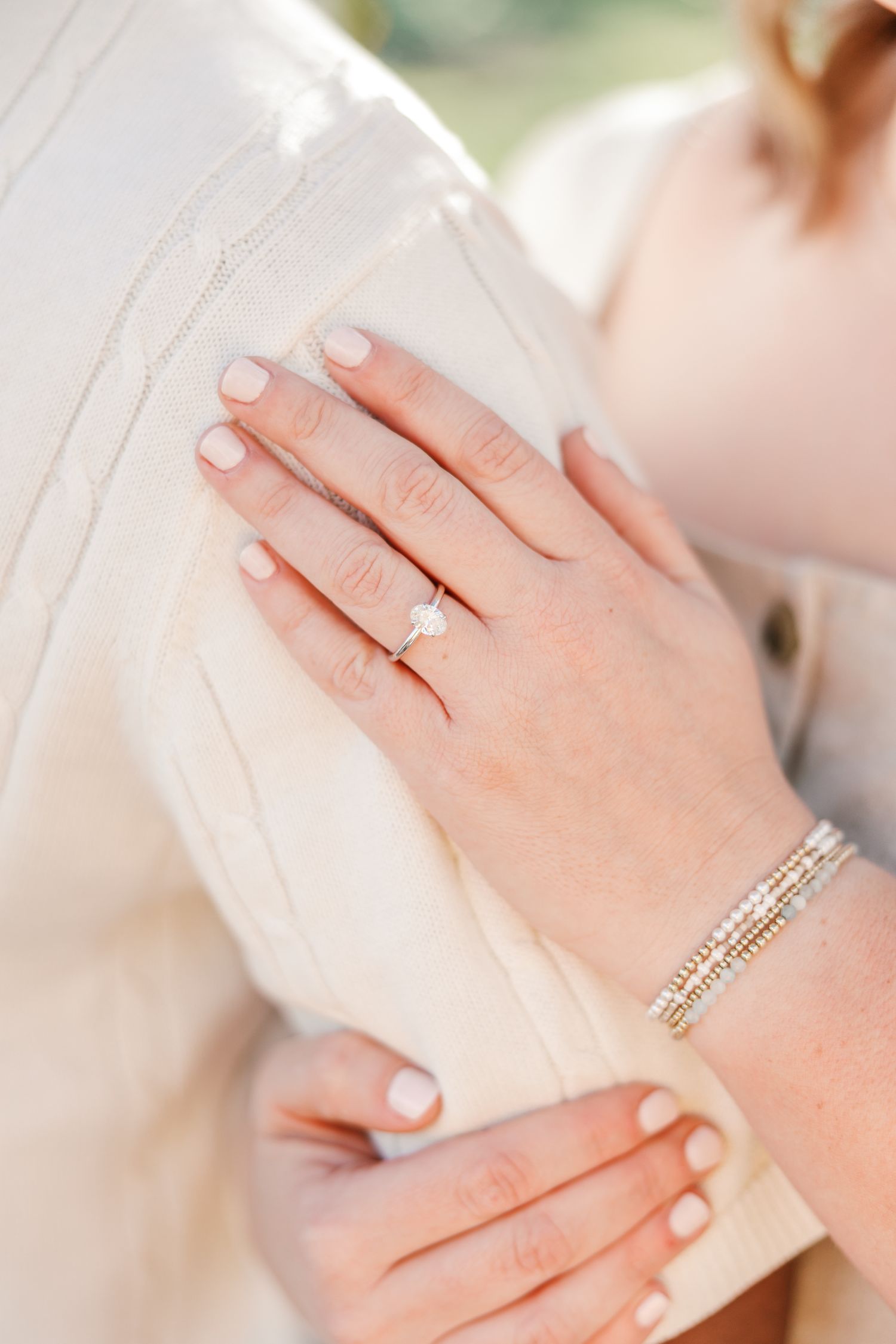 Close-up of hands showing an engagement ring and delicate bracelet against white fabric Matthews NC Engagement Photographer