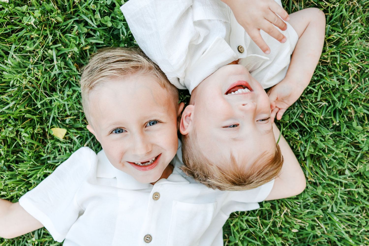 Children laying on grass wearing white outfits during outdoor photo session  in Clemmons NC  with a Family Photographer