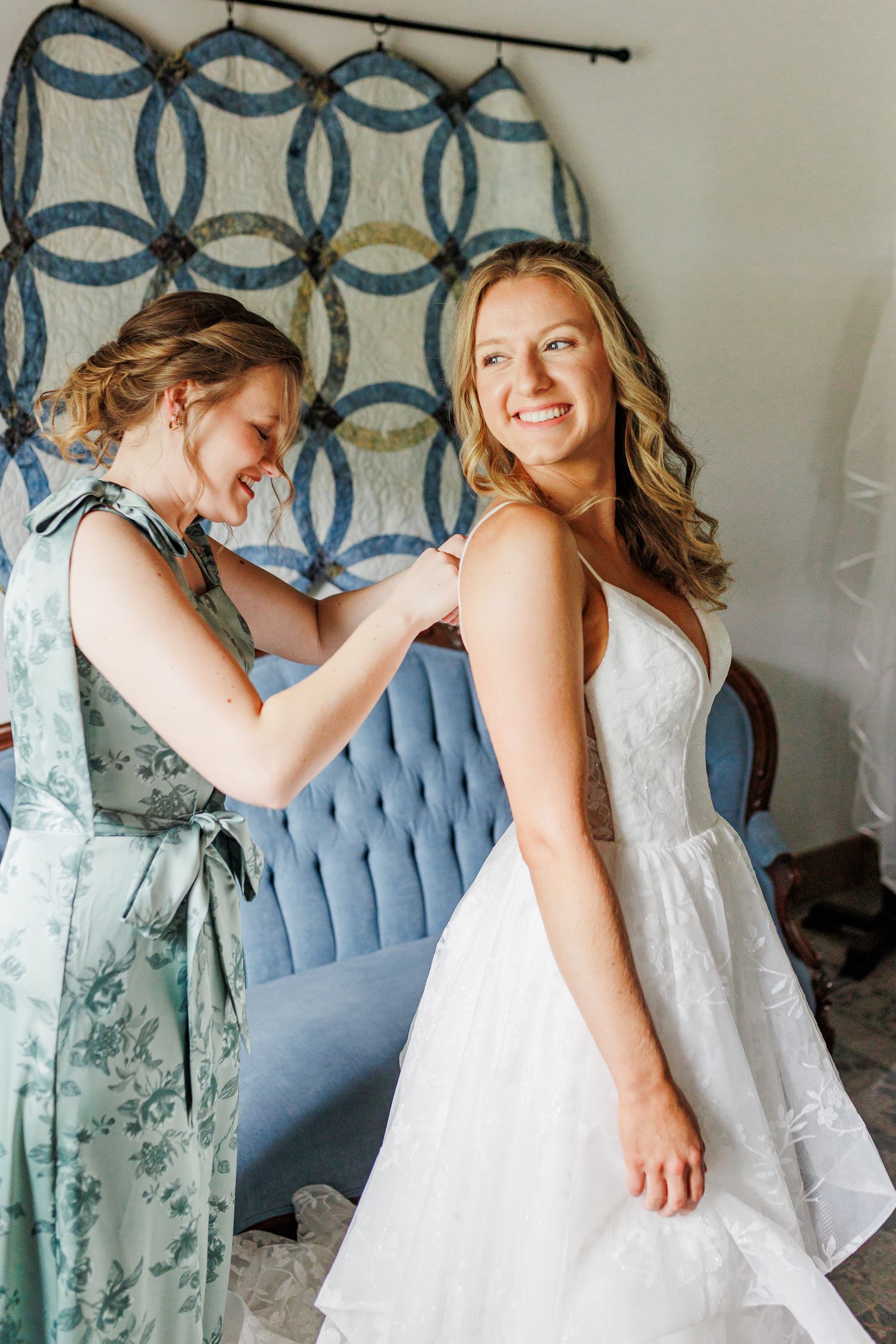 Bridesmaids in white dresses sitting on blue tufted couch against geometric patterned wall at Appalachian View Venue with Boone Photographer