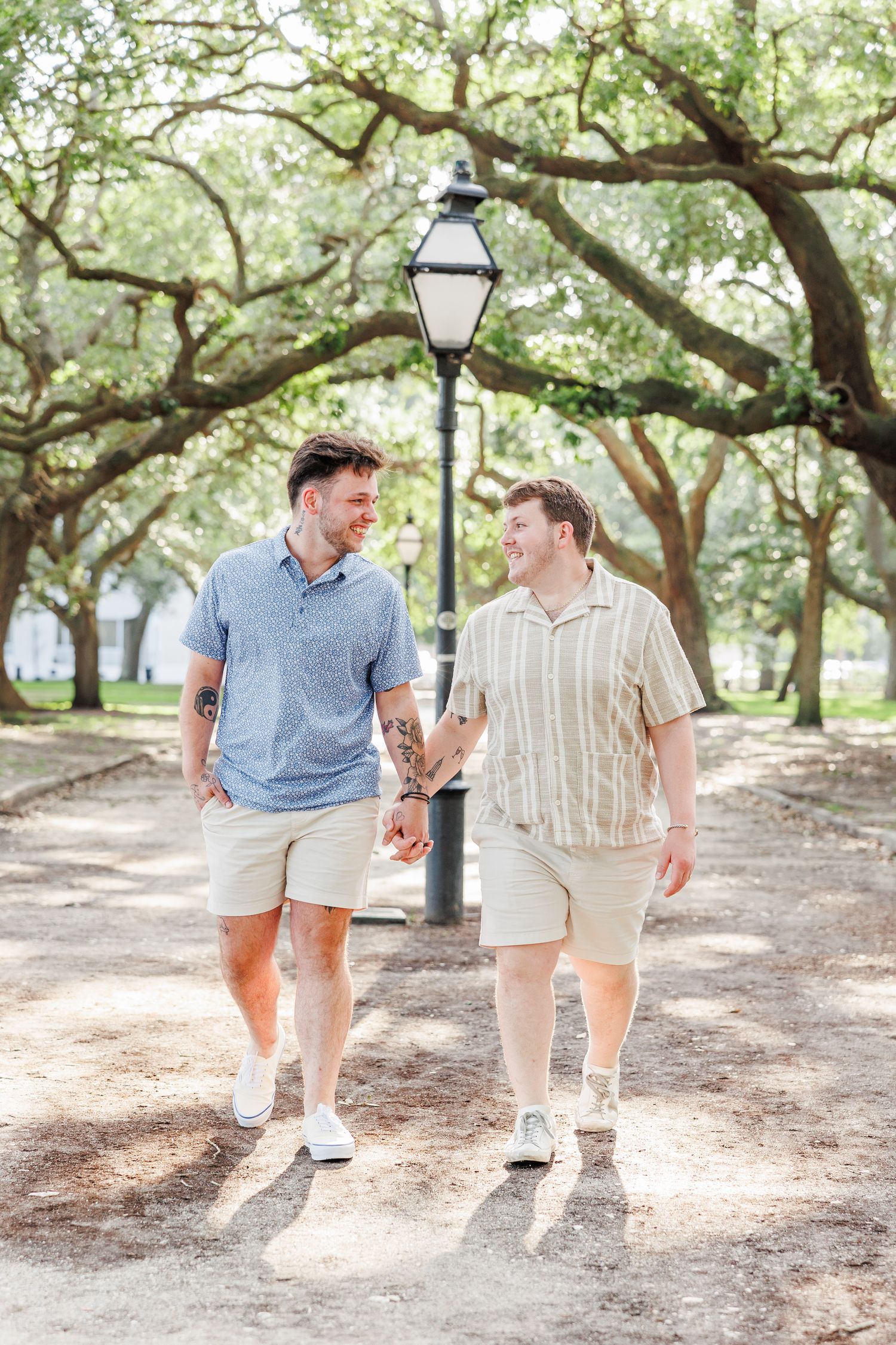 A couple walks hand in hand down a tree-lined path with a vintage lamppost with Charleston Engagement Photographer at Rainbow Row