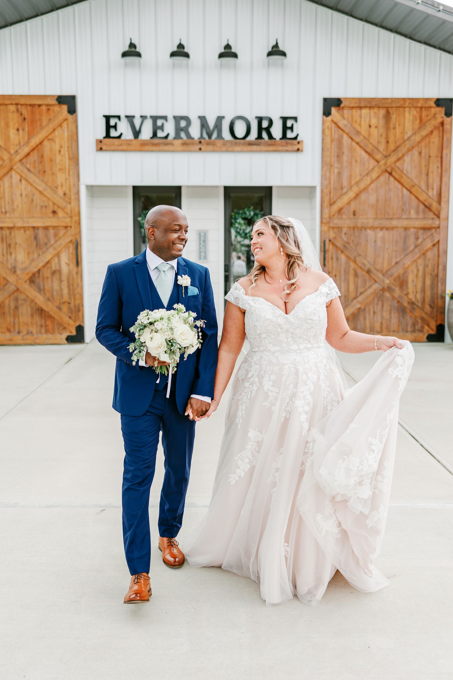 Newlyweds walking together in front of a modern white barn with wooden accents.