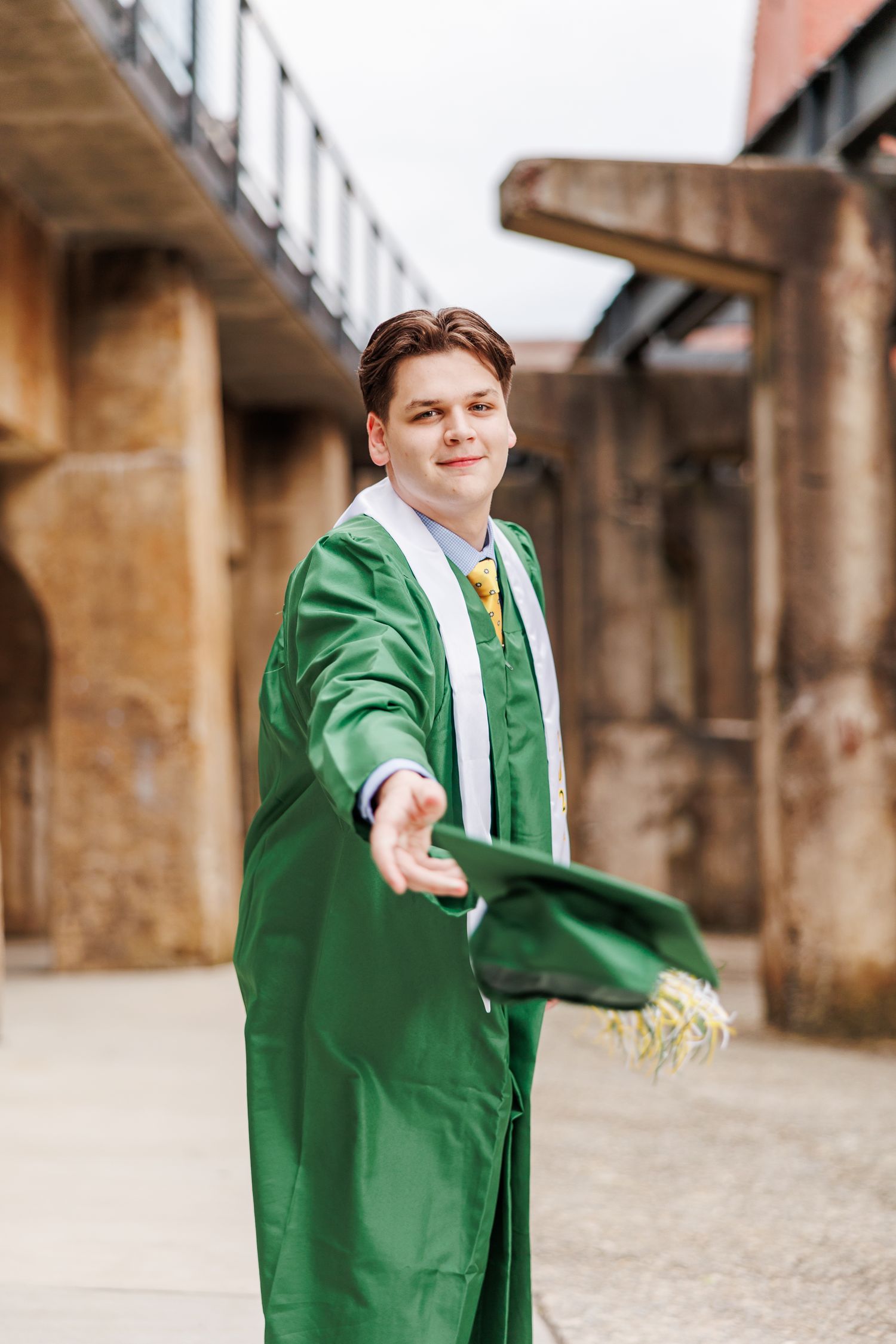 Graduate in green gown tossing cap in celebratory pose outdoors  for Senior Portrait Session in Winston Salem