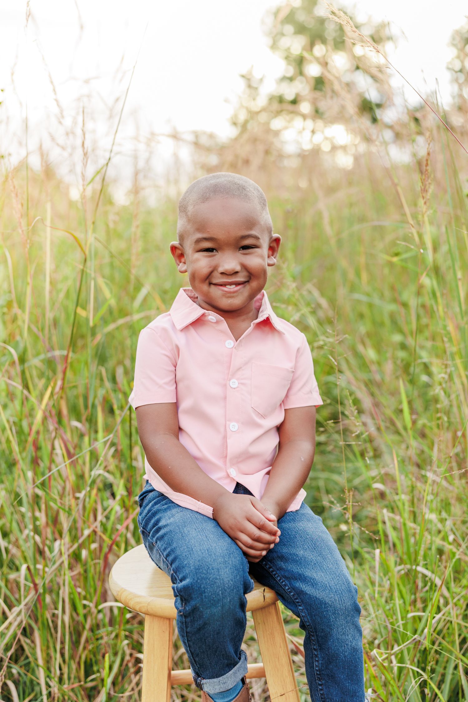 Child in pink polo shirt sits on wooden stool in grassy field iin Greensboro NC  with a Family Photographer