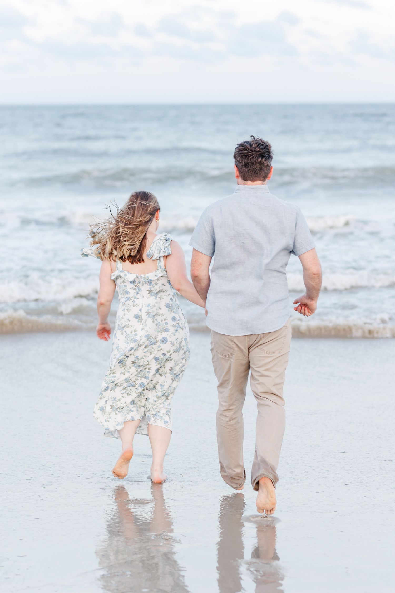 A couple runs joyfully together along the shoreline of a beach at Fort Fisher with Wilmington North Carolina Wedding Photographer