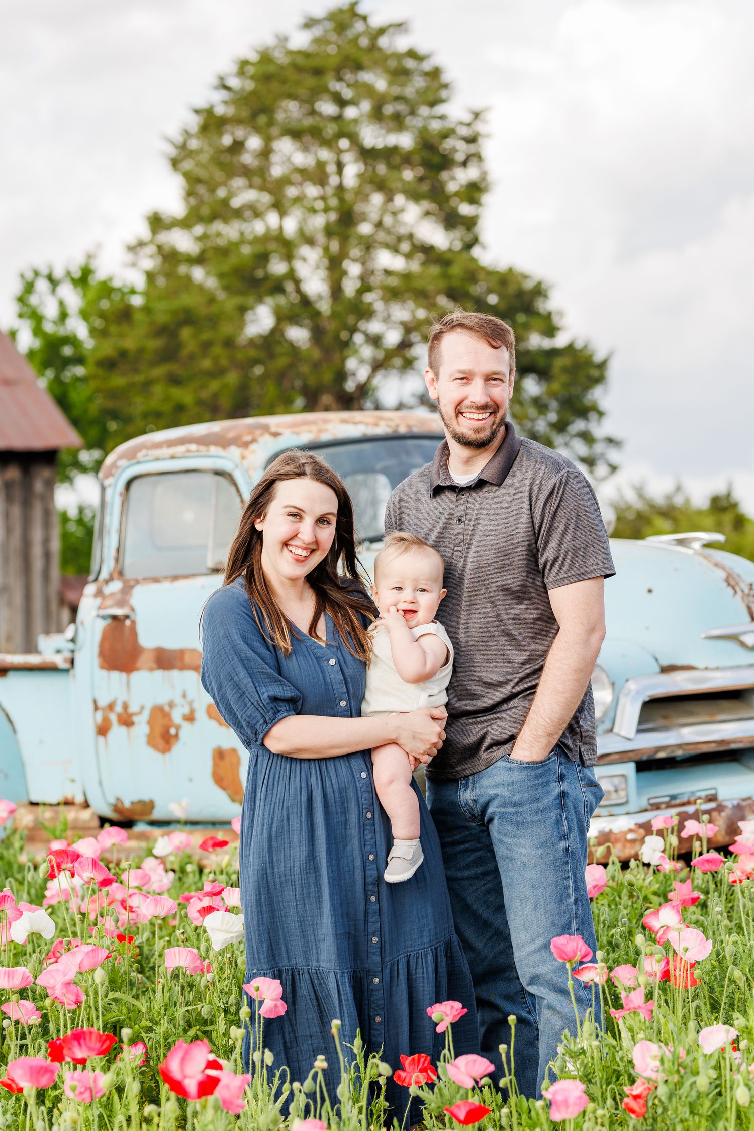 Family poses for photos in a poppy field with vintage blue truck in background in Winston Salem NC  with a Family Photographer
