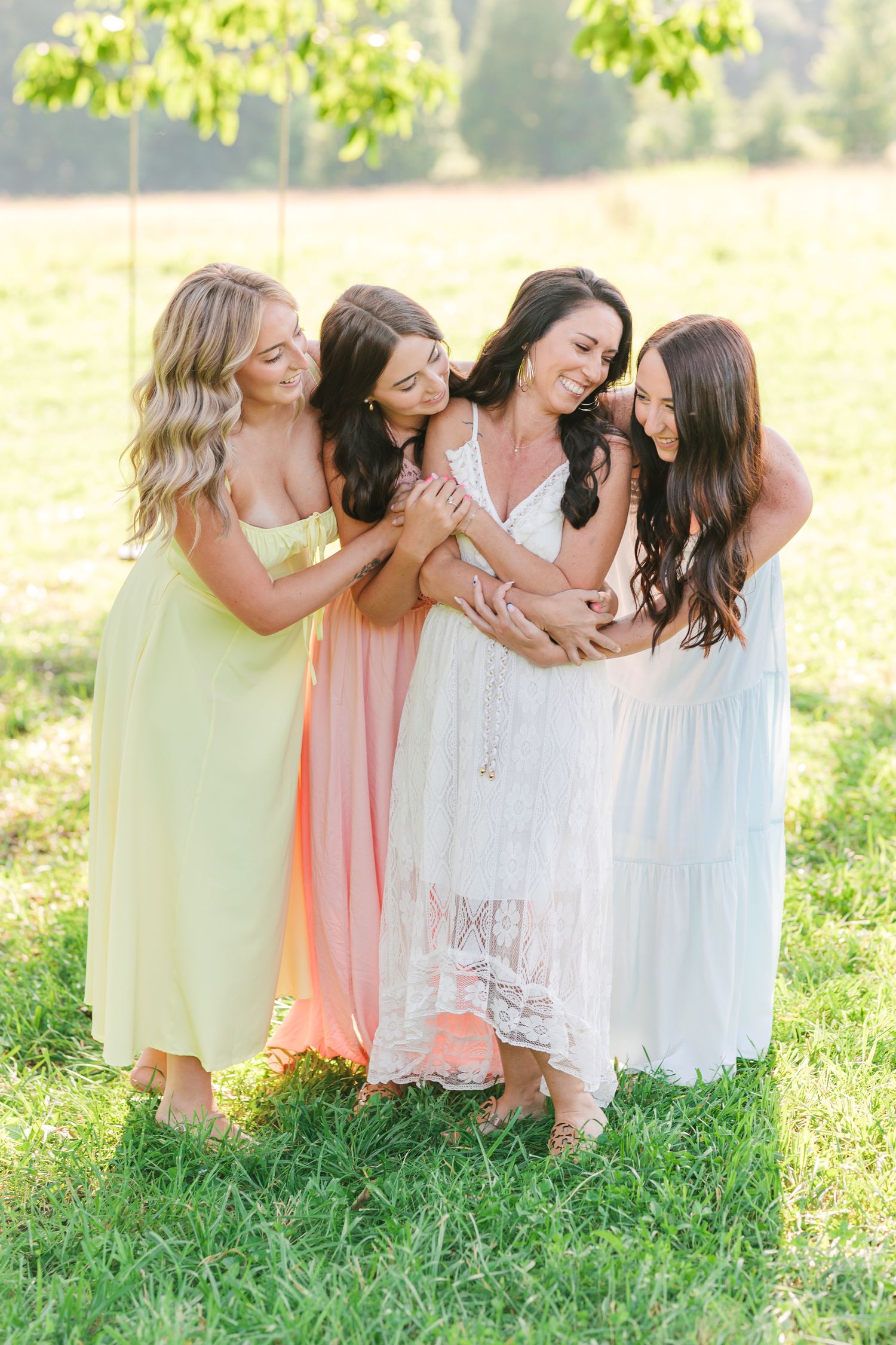 Friends in pastel dresses sitting together on grass in a candid moment in Greensboro with a Family Photographer