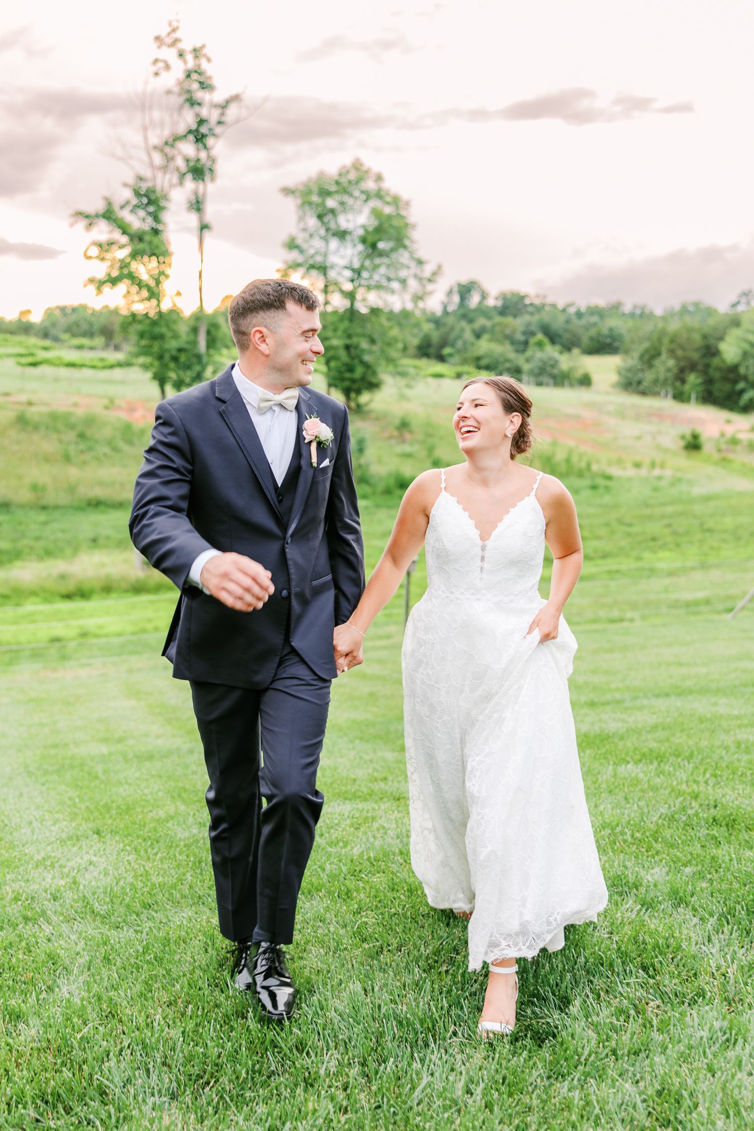 A couple shares joyful moments while walking through green grass on their wedding day with Winston Salem Wedding Photographer