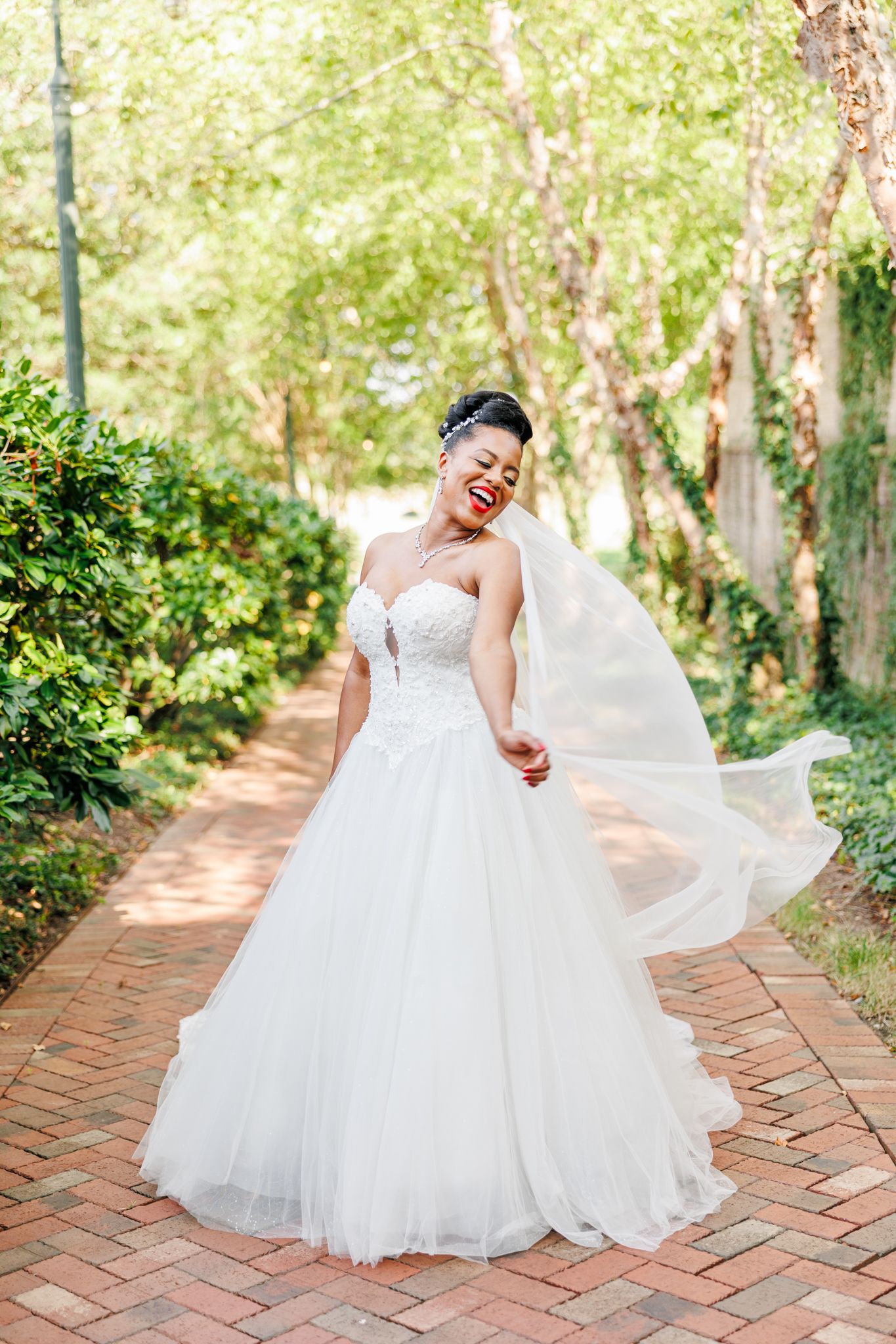 Person in flowing white wedding gown twirling on brick pathway surrounded by greenery at the Grandover Resort  with NC Wedding Photographer
