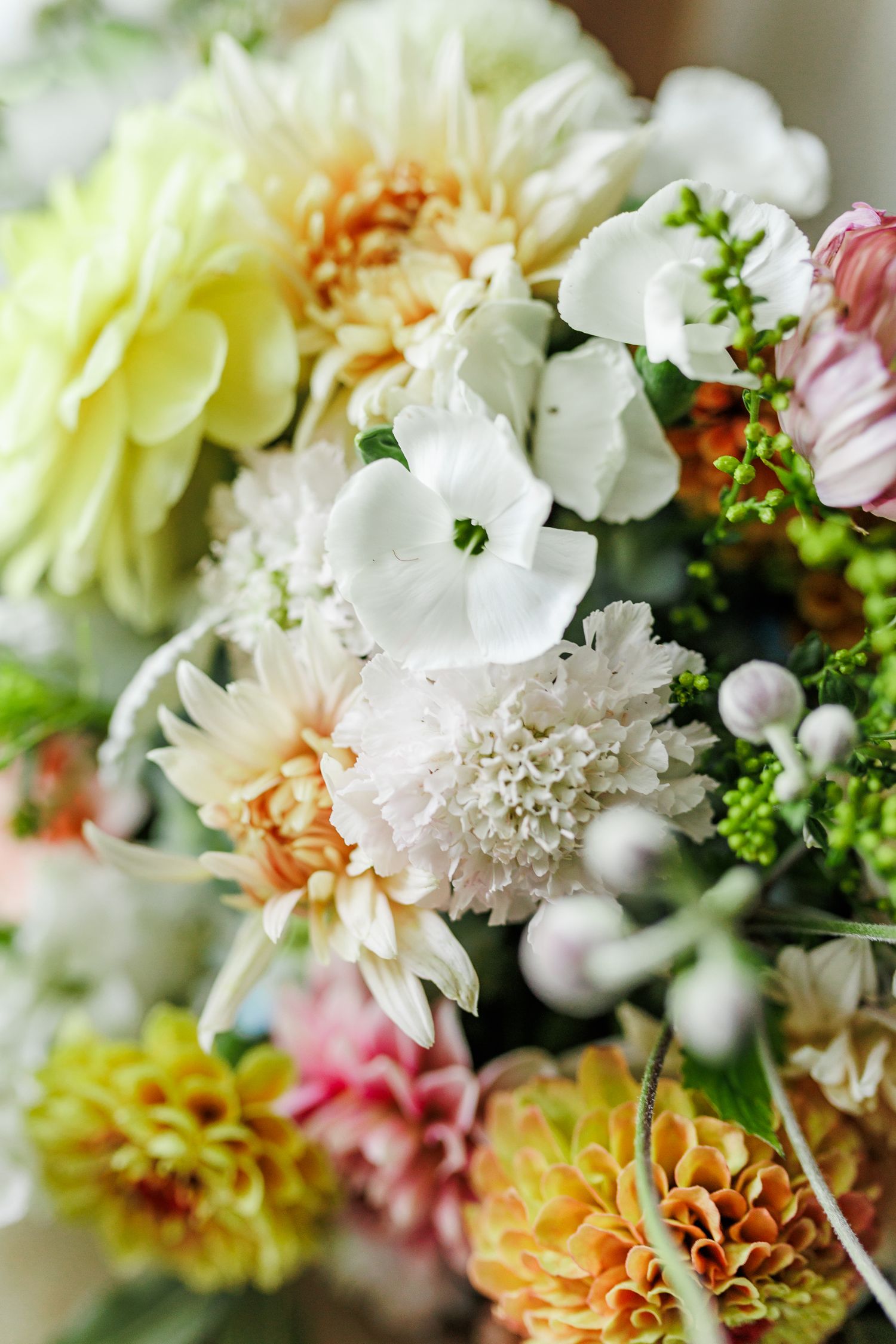 Close-up of pastel wedding bouquet with white, pink and peach flowers mixed with greenery.