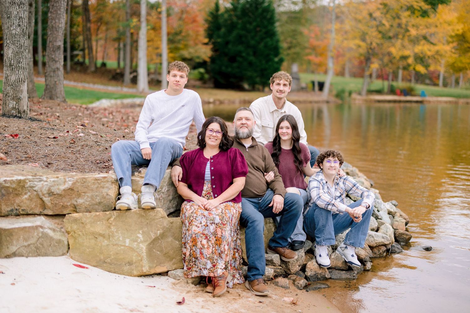 Group enjoying a relaxing moment by a lake surrounded by fall colors and trees in Greensboro with a Family Photographer