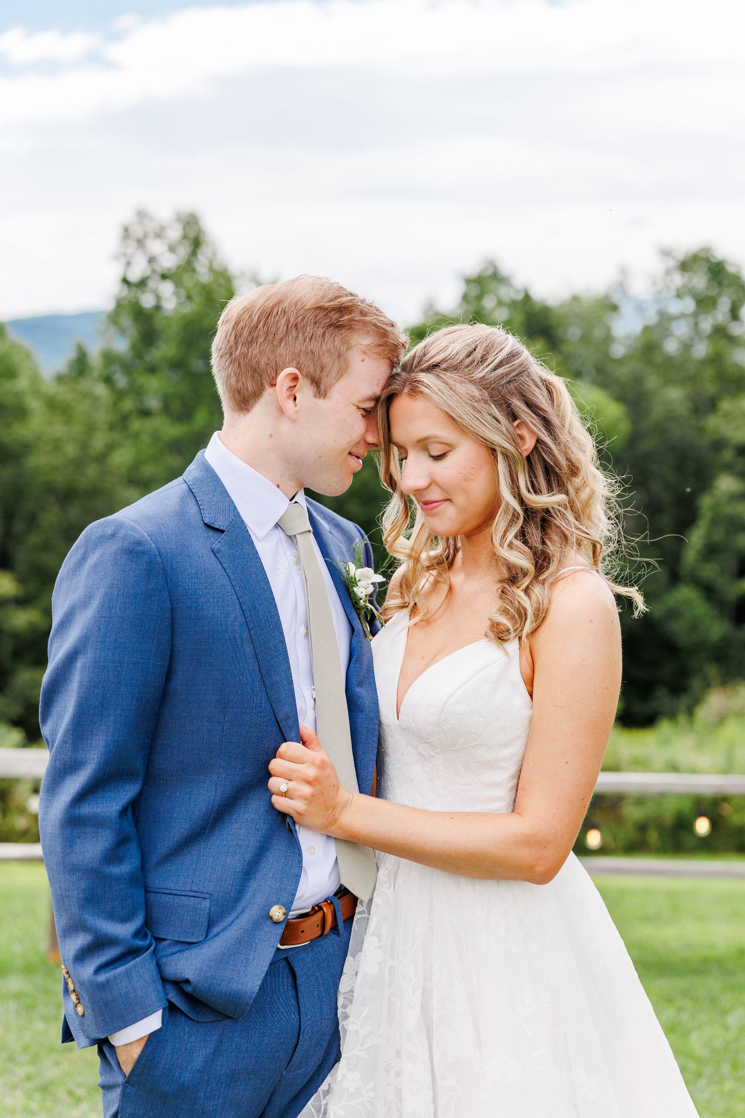 Romantic wedding portrait in outdoor setting with couple in blue suit and white dress.