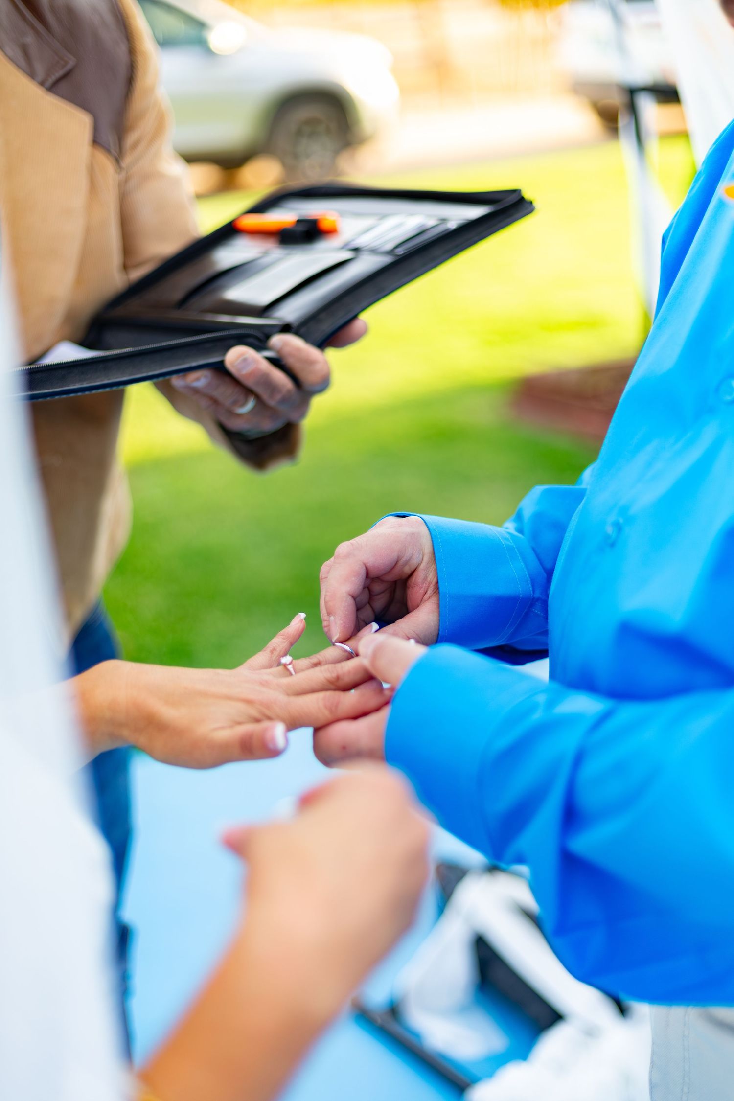 A nurse places a ring on a patient's finger outdoors while a person with a clipboard observes.