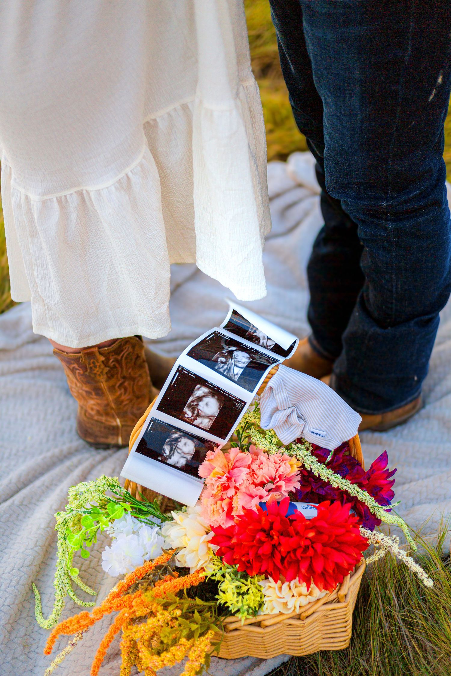 Pregnancy announcement with ultrasound photos in a flower basket, couple standing on blanket wearing cowboy boots and jeans.
