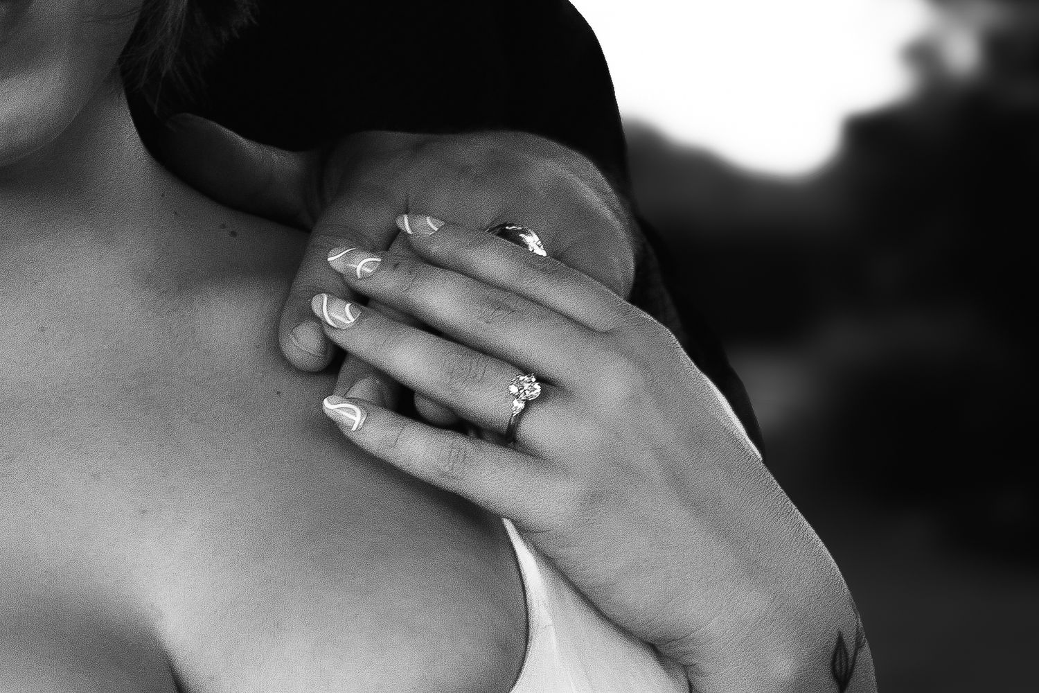 Black and white close-up of hand with engagement ring resting on shoulder.