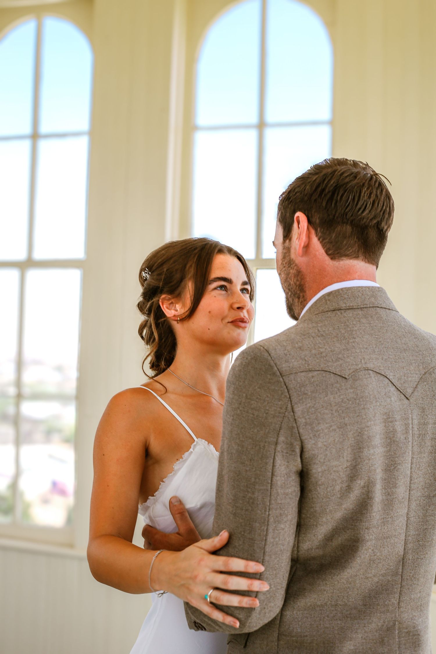 Bride and groom share an intimate first dance moment, with the bride gazing up lovingly in a white dress.