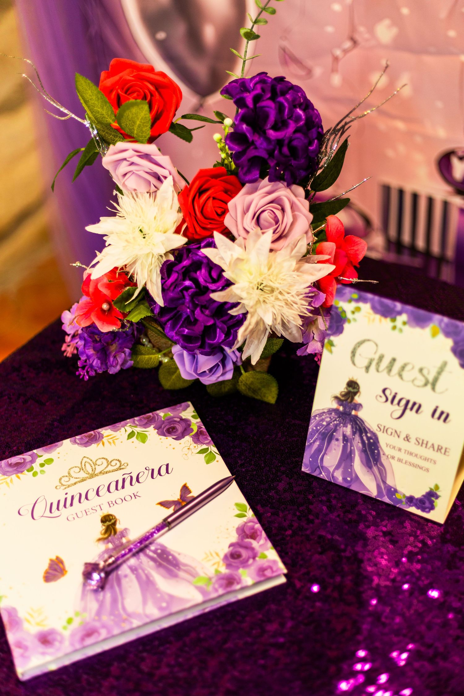 Quinceañera guest book and sign-in table with purple sequin cloth, floral arrangement, and decorative sign.