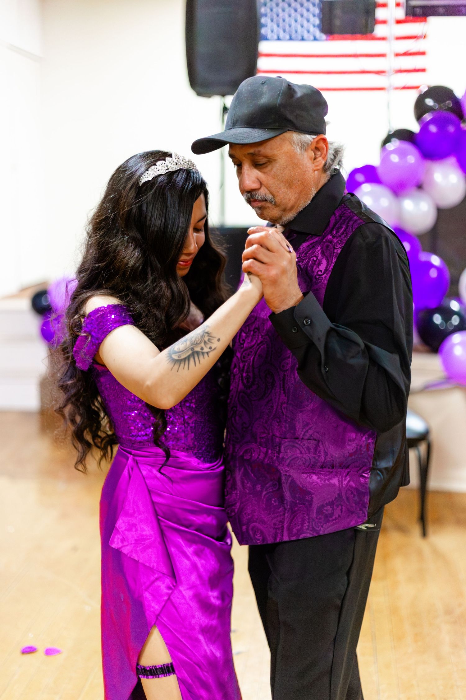 A young woman in a purple gown dances with an older man in a purple vest at a quinceañera celebration.