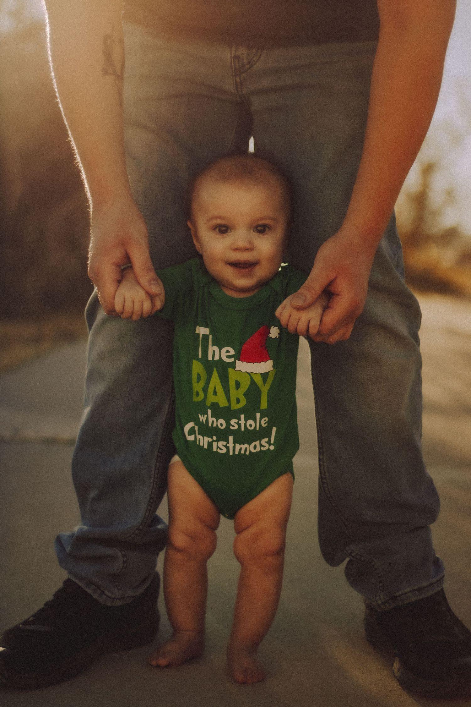 Smiling baby in The Baby Who Stole Christmas green onesie standing.