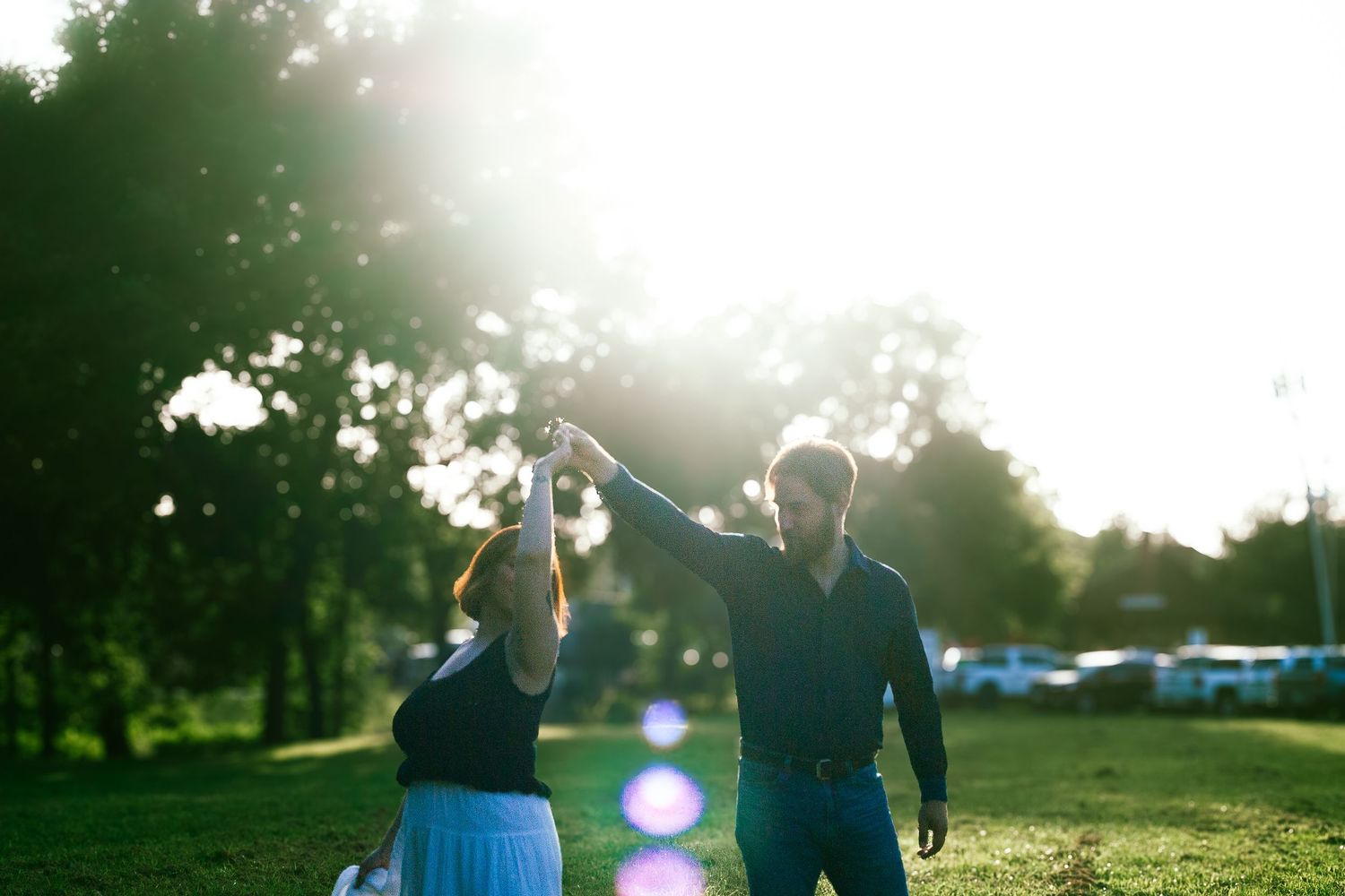 Couple dancing and holding hands in sunlit green park with bright lens flare.