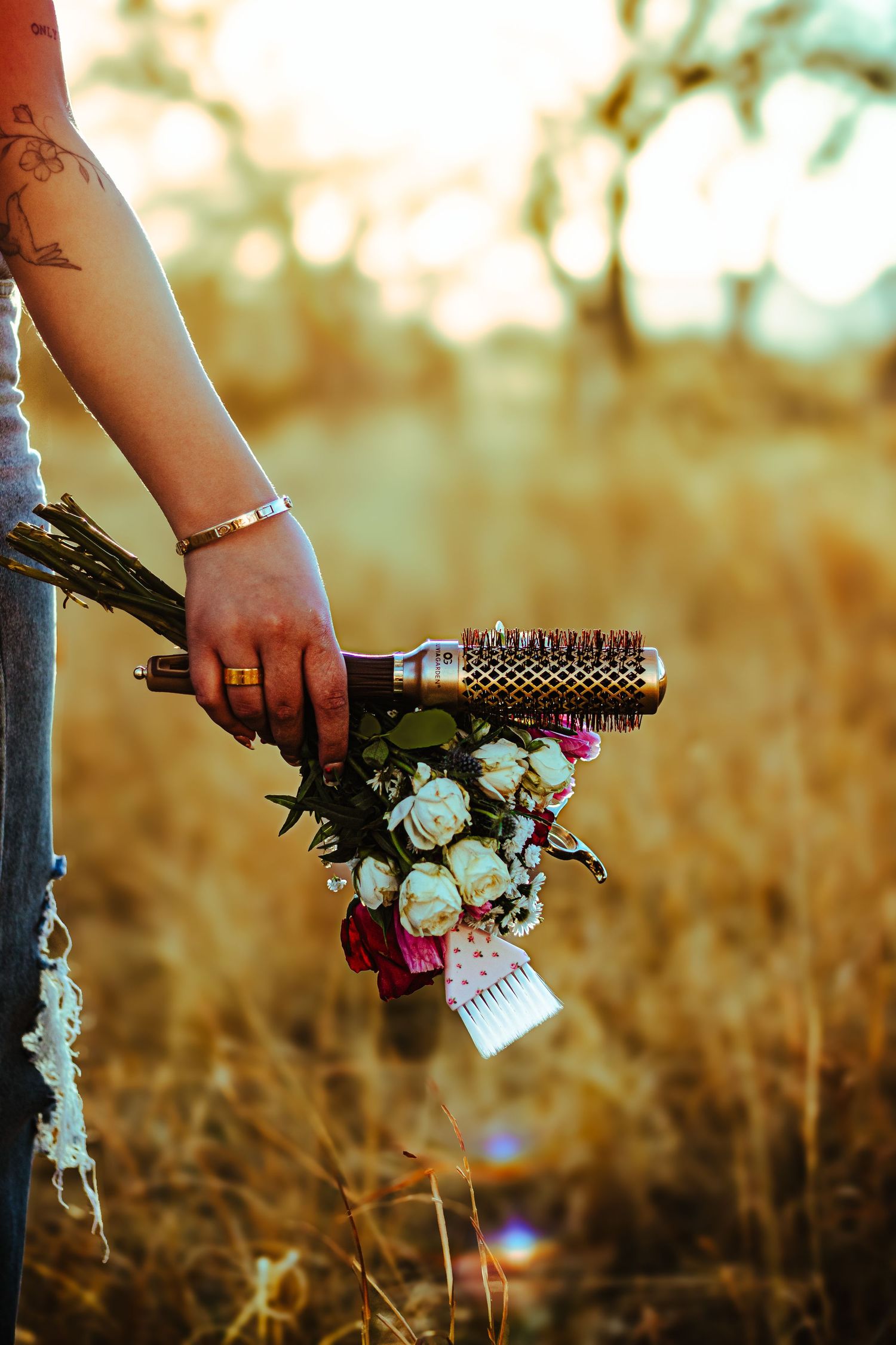 Hand holding a round hair brush bouquet with white roses in a golden field at sunset.