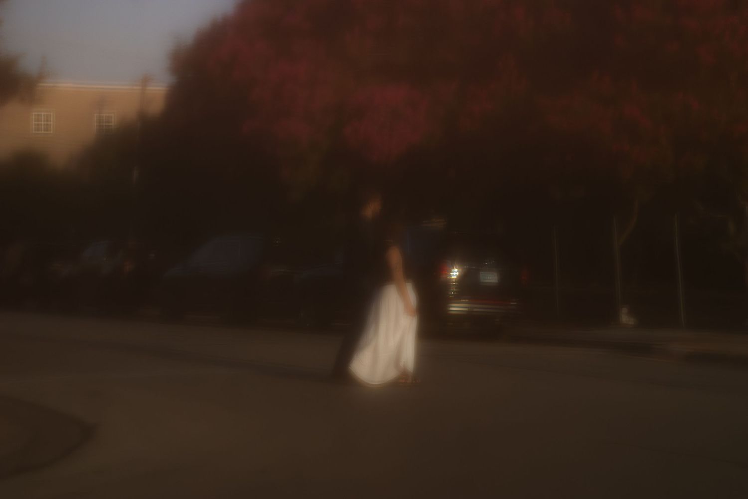Blurry artistic photo of a person in a white dress walking on a dark street at dusk near autumn trees.