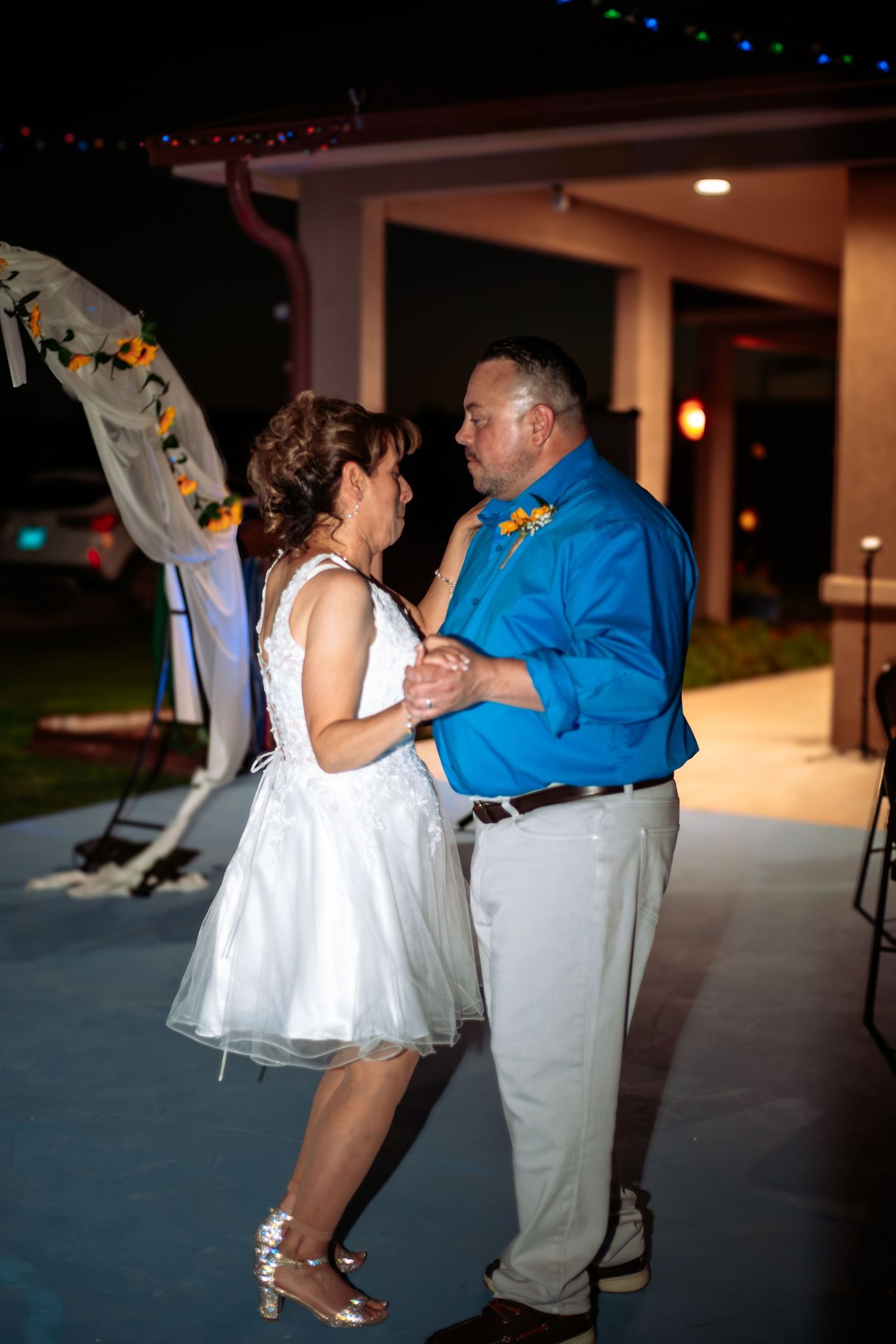 Bride and groom share first dance at night under string lights at outdoor wedding reception.
