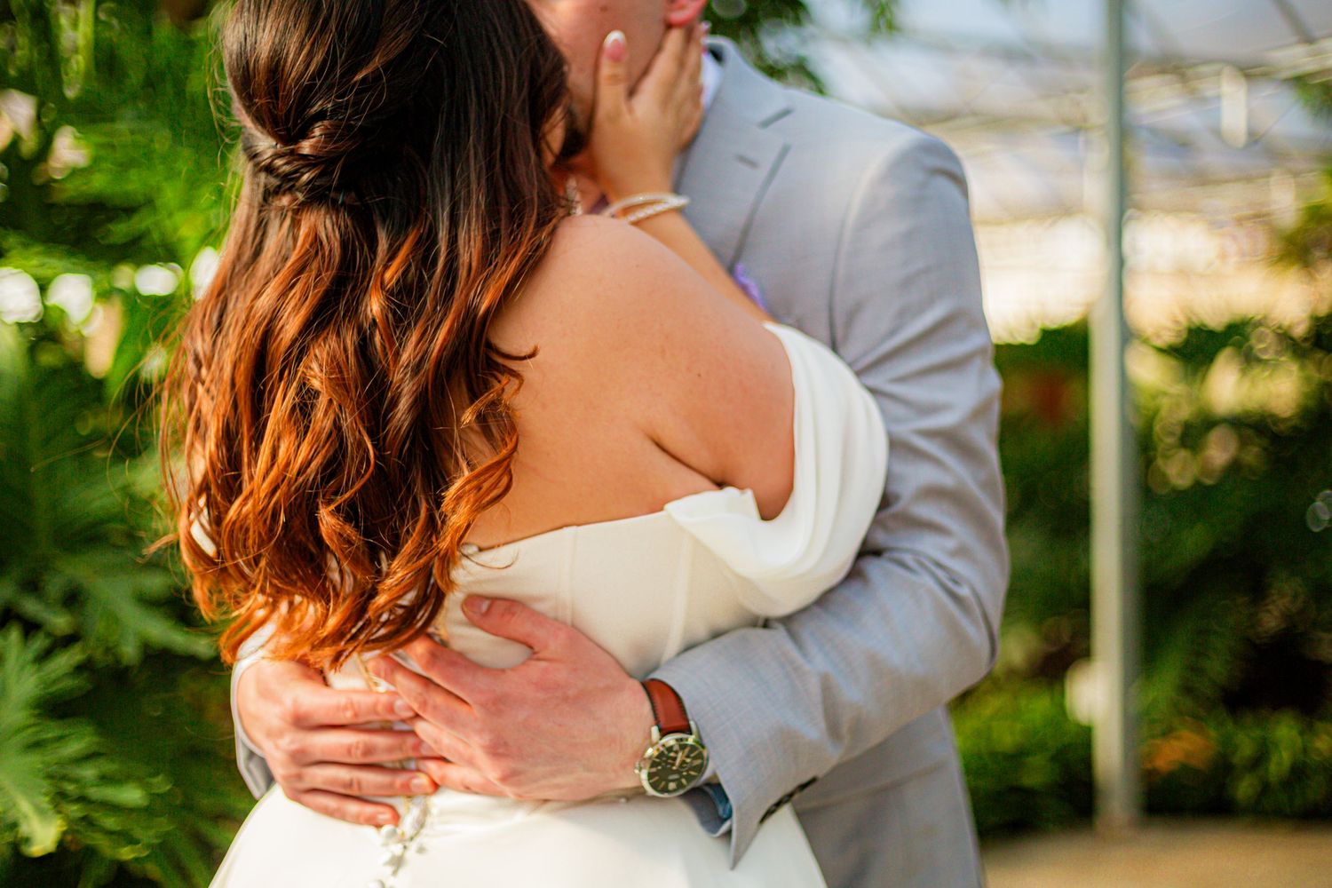 Bride and groom sharing a romantic embrace outdoors, surrounded by lush greenery at their wedding.