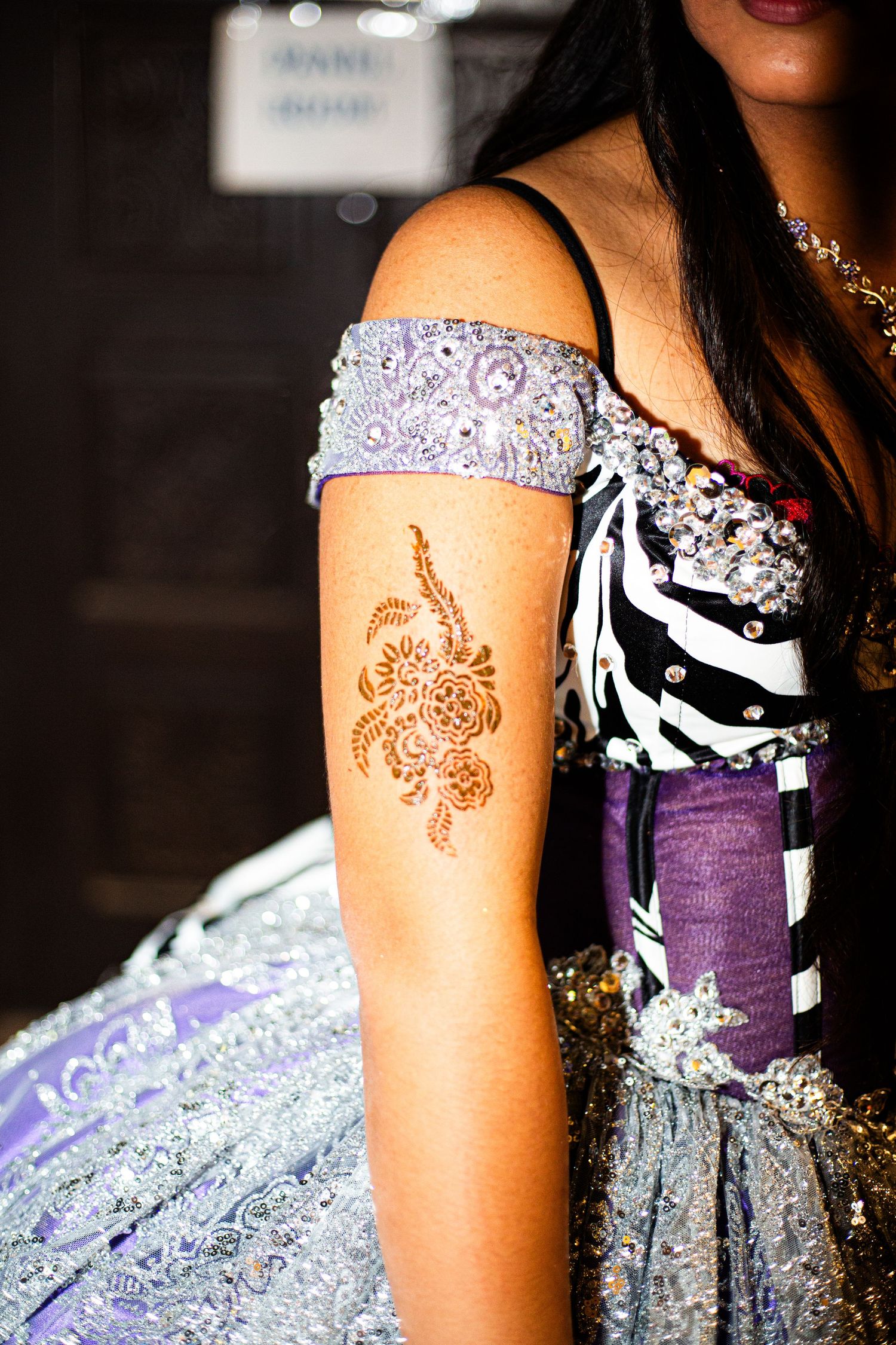 Woman in lavender off-shoulder gown with intricate henna tattoo on her arm, adorned with jeweled embellishments.