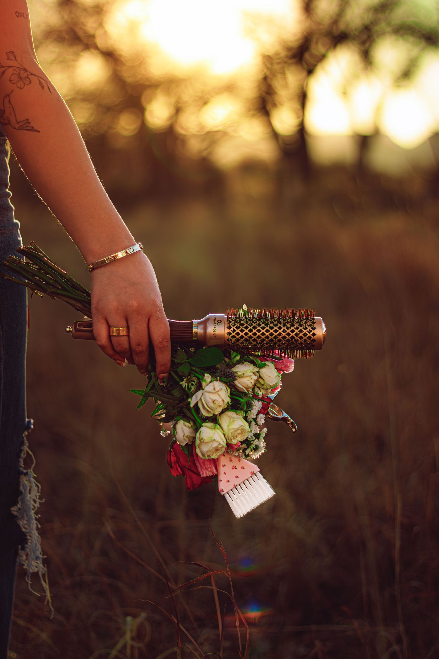 Hand holding a floral bouquet with a round hair brush at golden hour in a field.