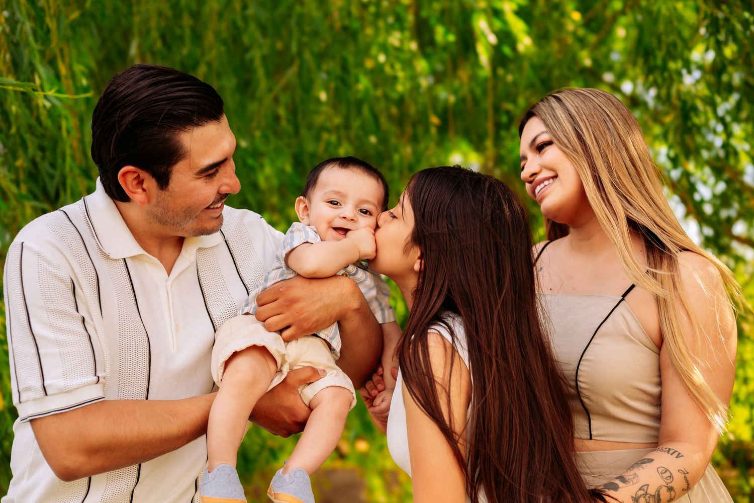Happy family with parents and two children sharing a joyful moment outdoors near green willow trees.