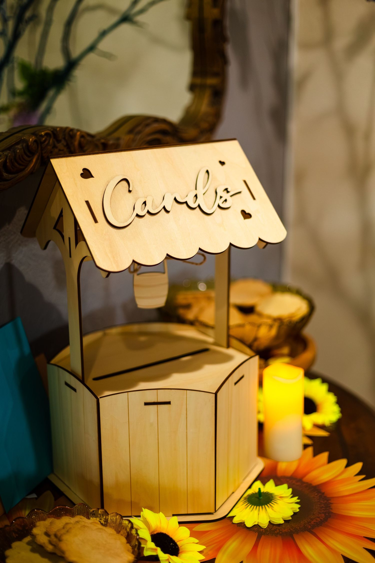 Rustic wooden card box with laser-cut Cards sign and scalloped roof, decorated with sunflowers and candles at a wedding reception.