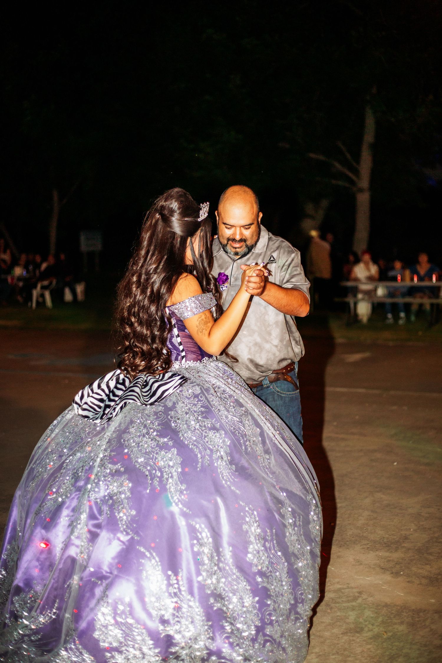 A father and daughter share a dance at a quinceañera celebration, with the girl wearing a purple ball gown.