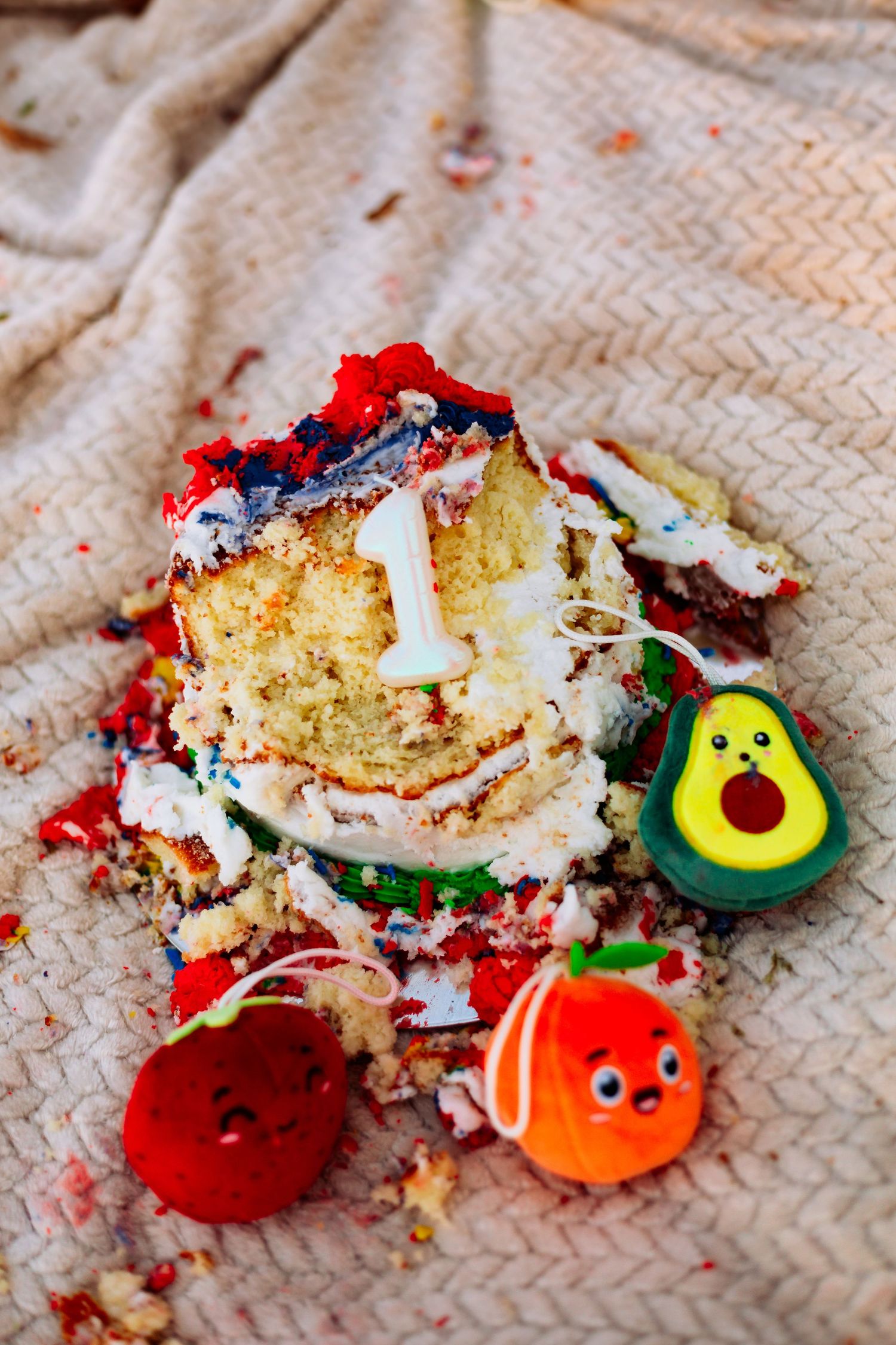 Smashed first birthday cake with number one candle surrounded by cute avocado and fruit decorations.