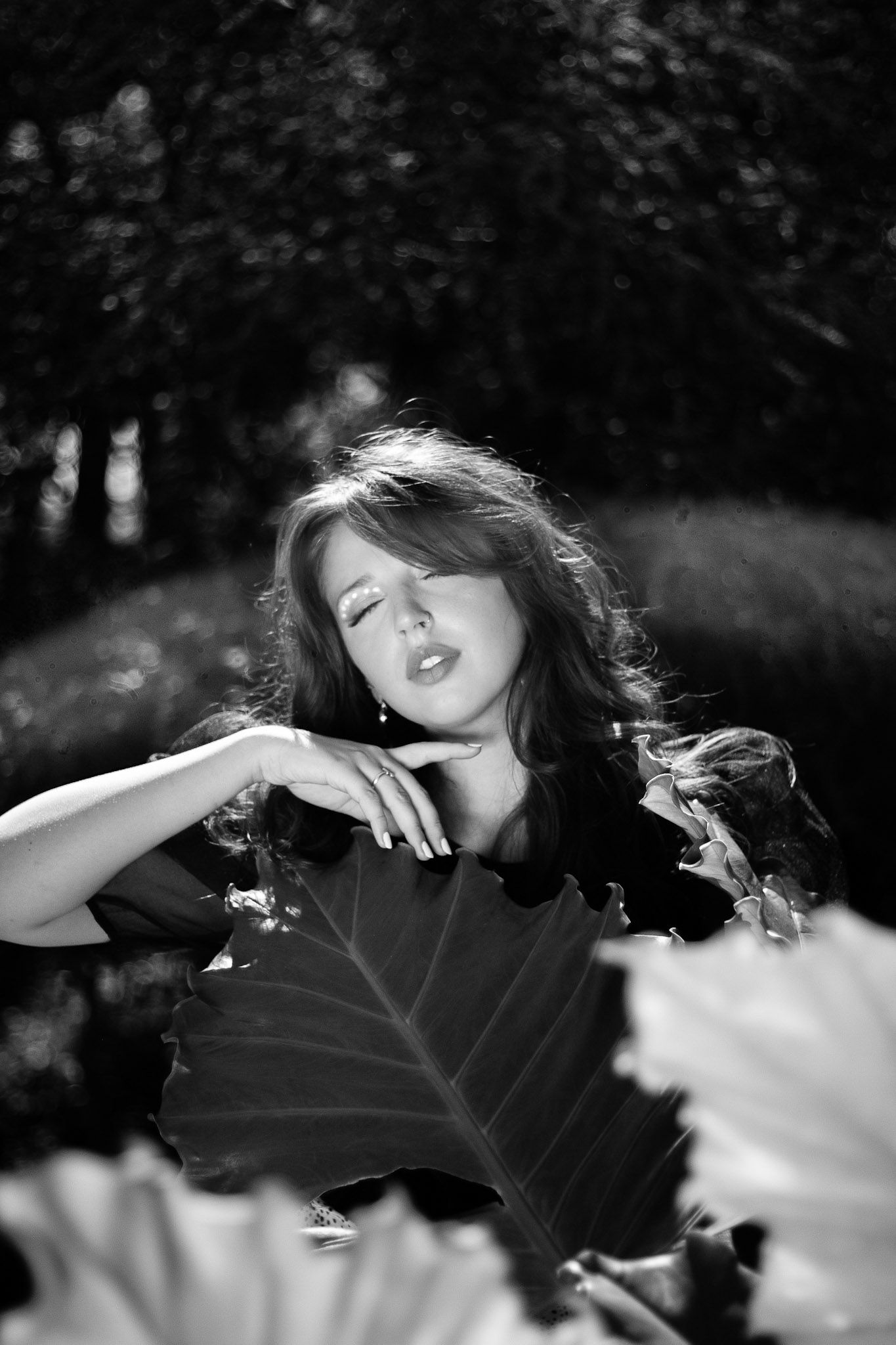 Black and white portrait of a woman posing gracefully among large tropical leaves in a garden.