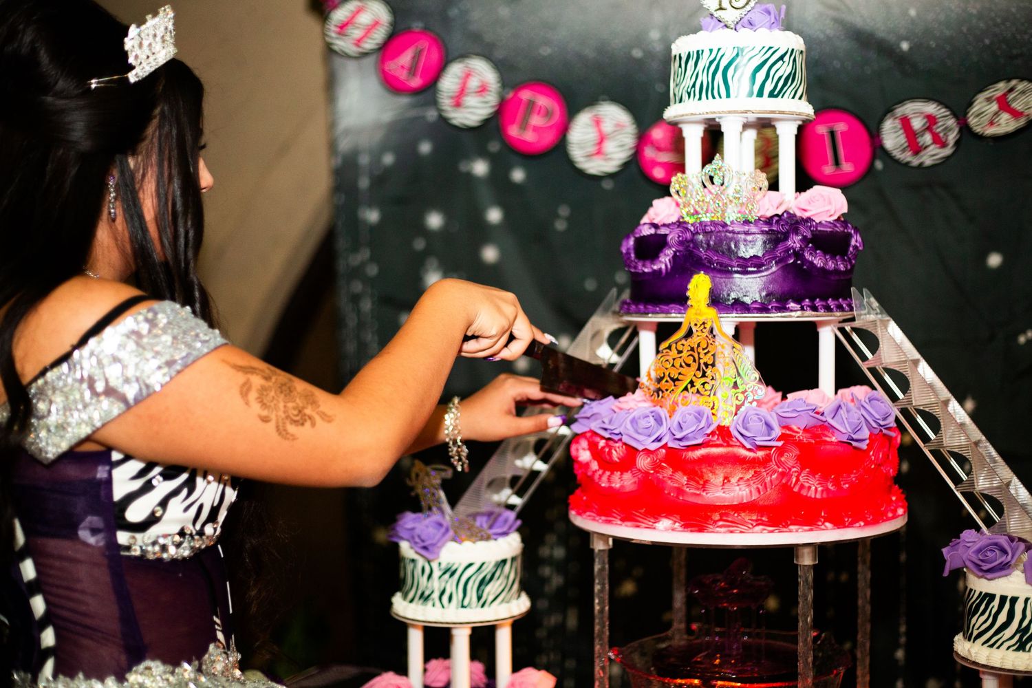 Woman cutting a multi-tiered birthday cake with colorful decorations at a birthday party celebration.