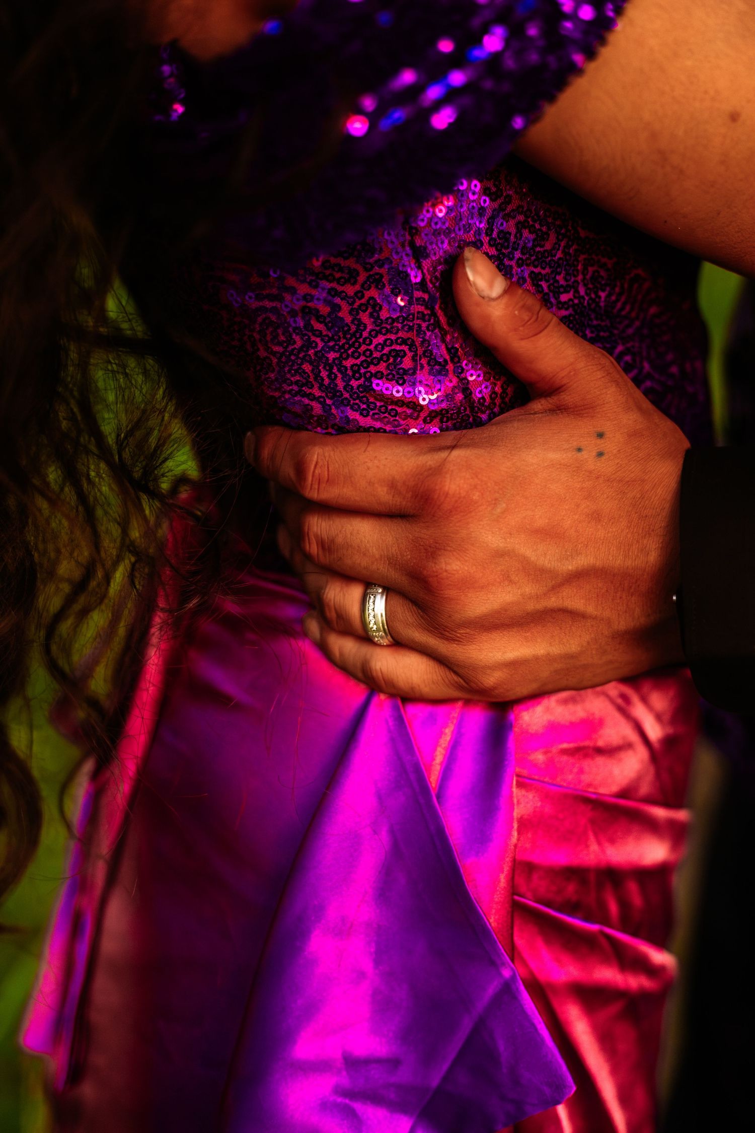 Close-up of a hand with a diamond ring resting on a woman's waist in a purple sequined dress.