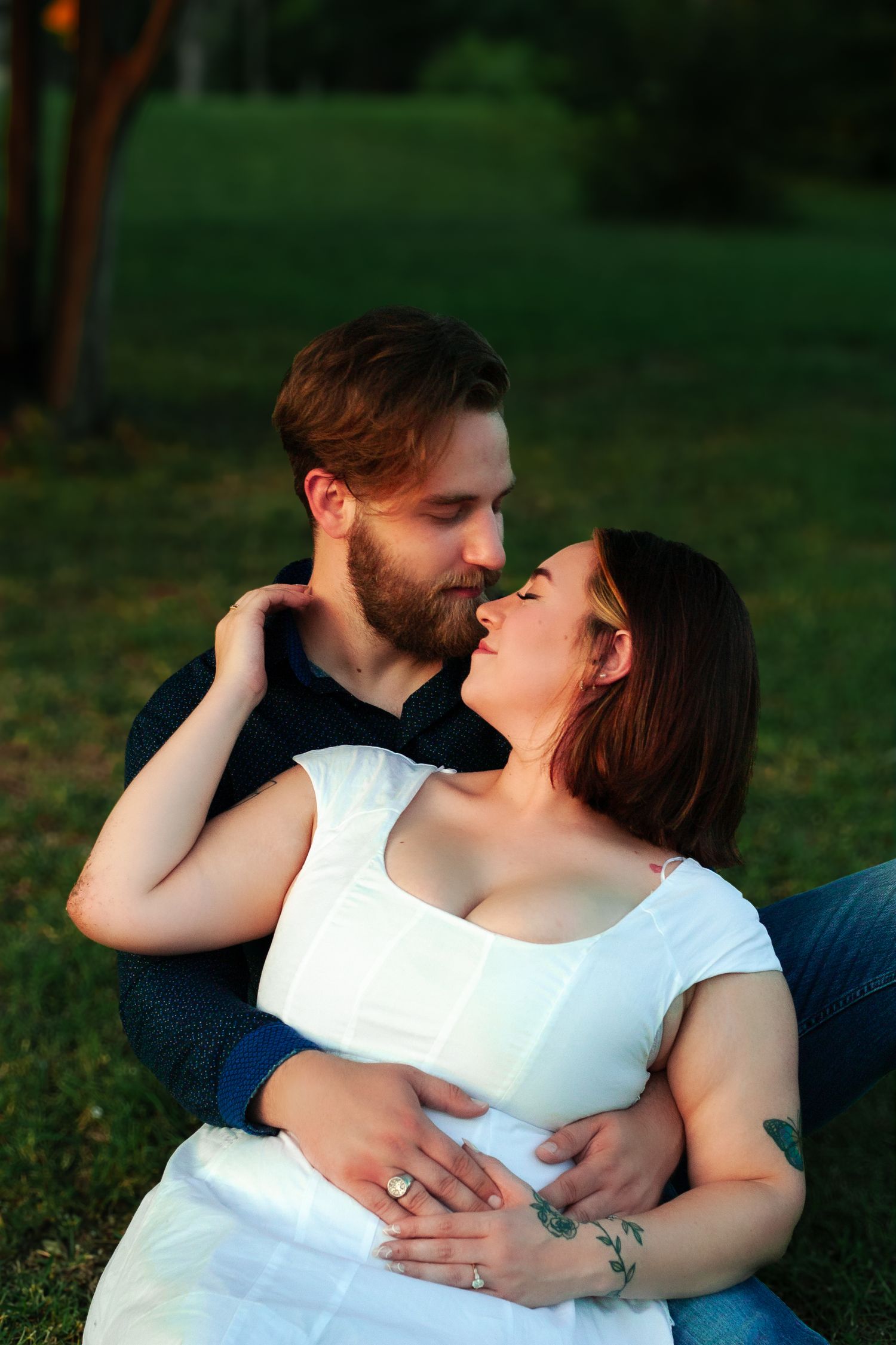 Romantic couple sitting on grass at sunset, embracing and gazing at each other lovingly.