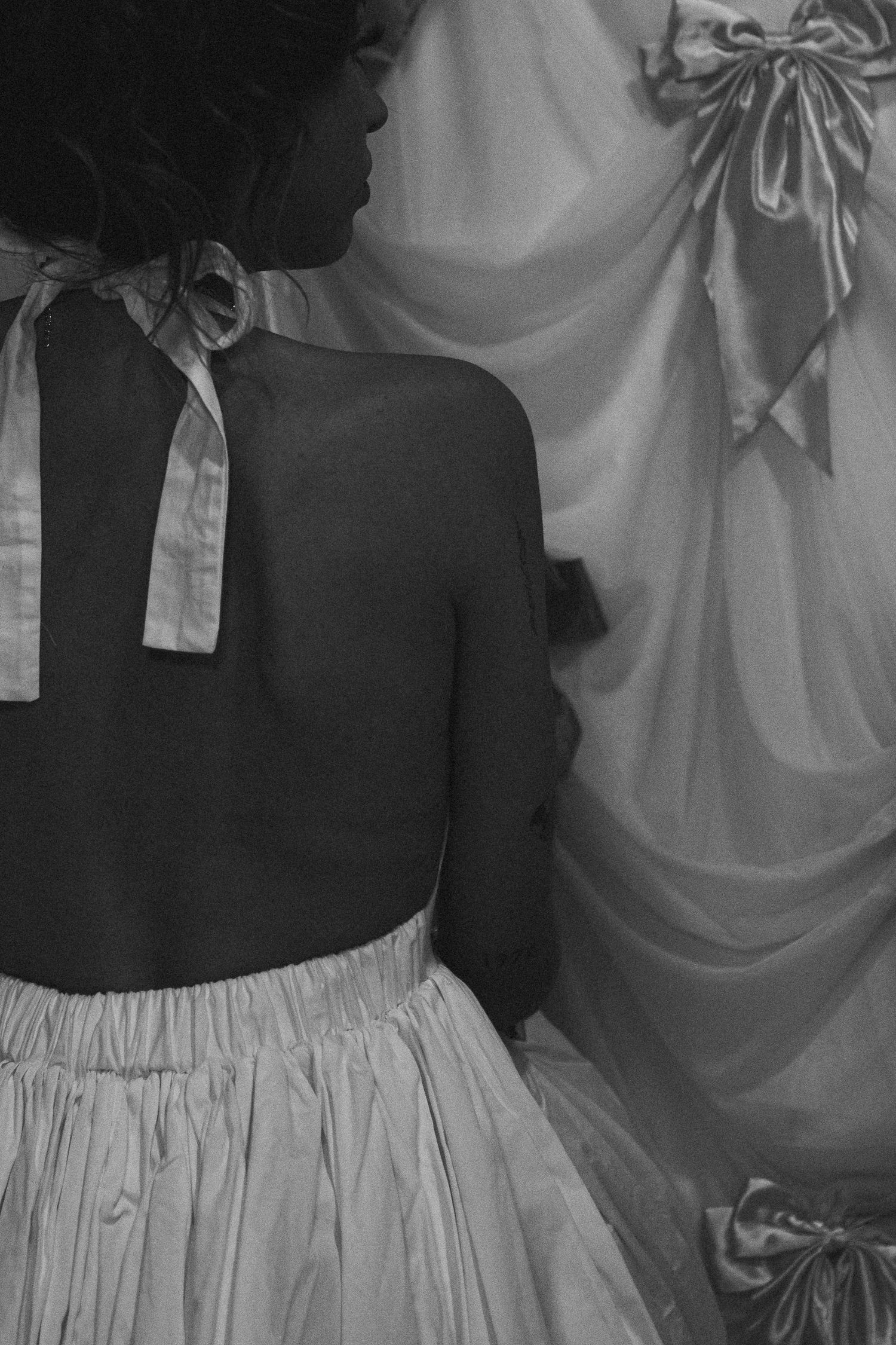 Black and white back view of woman in white halter dress with bow detail.