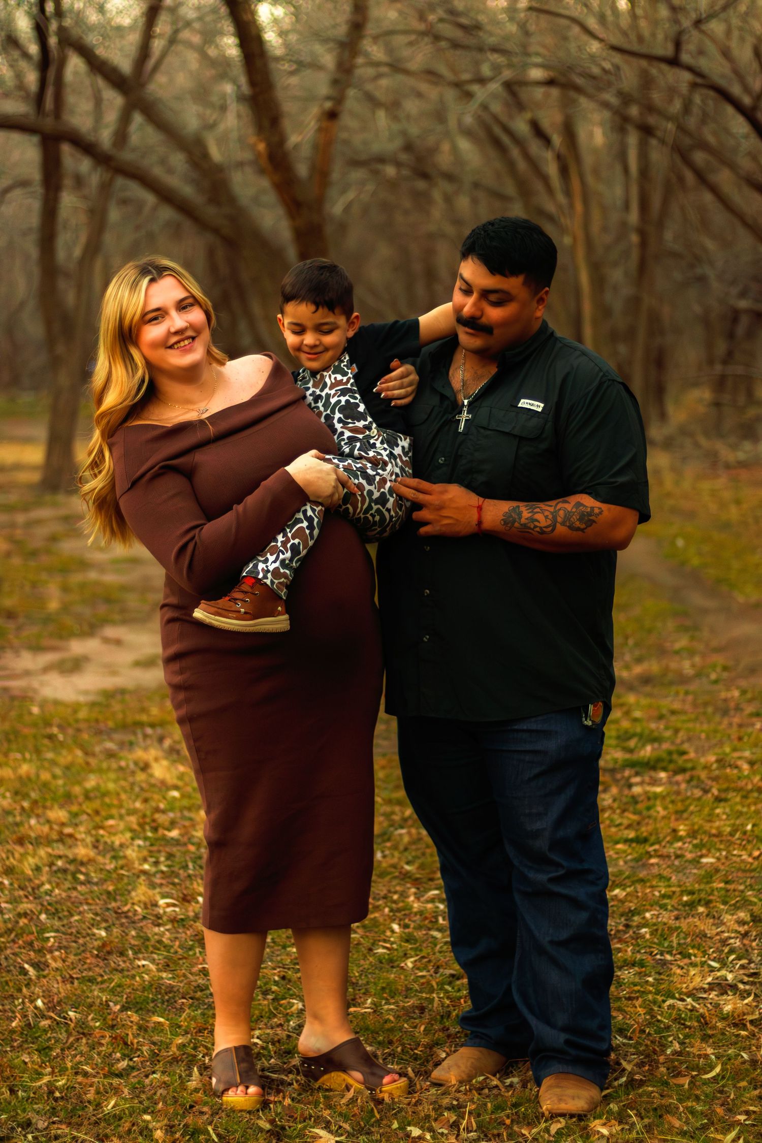 Happy pregnant family with young child posing in autumn forest setting.